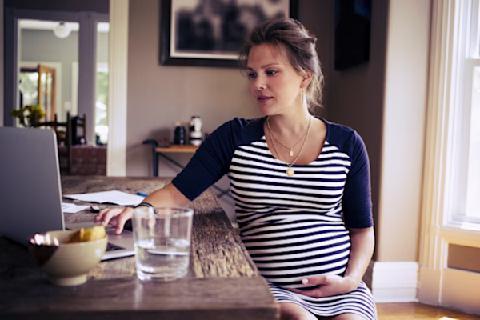 Pregnant woman holding belly while working on laptop at home Pregnant woman holding belly while working on laptop at home