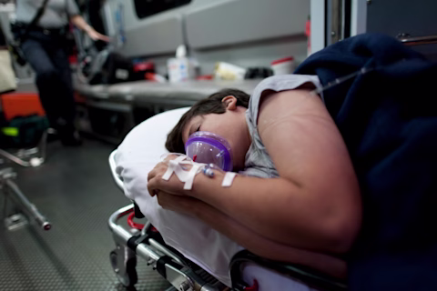 A person laying on an ambulance stretcher on their side, while wearing an oxygen mask