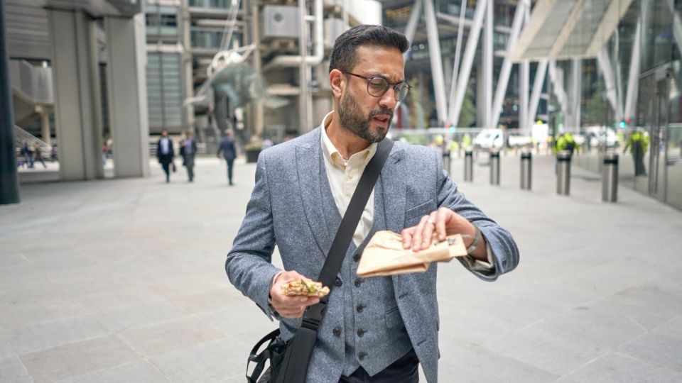A man walking from the office in his lunch break and checking the time as he eats