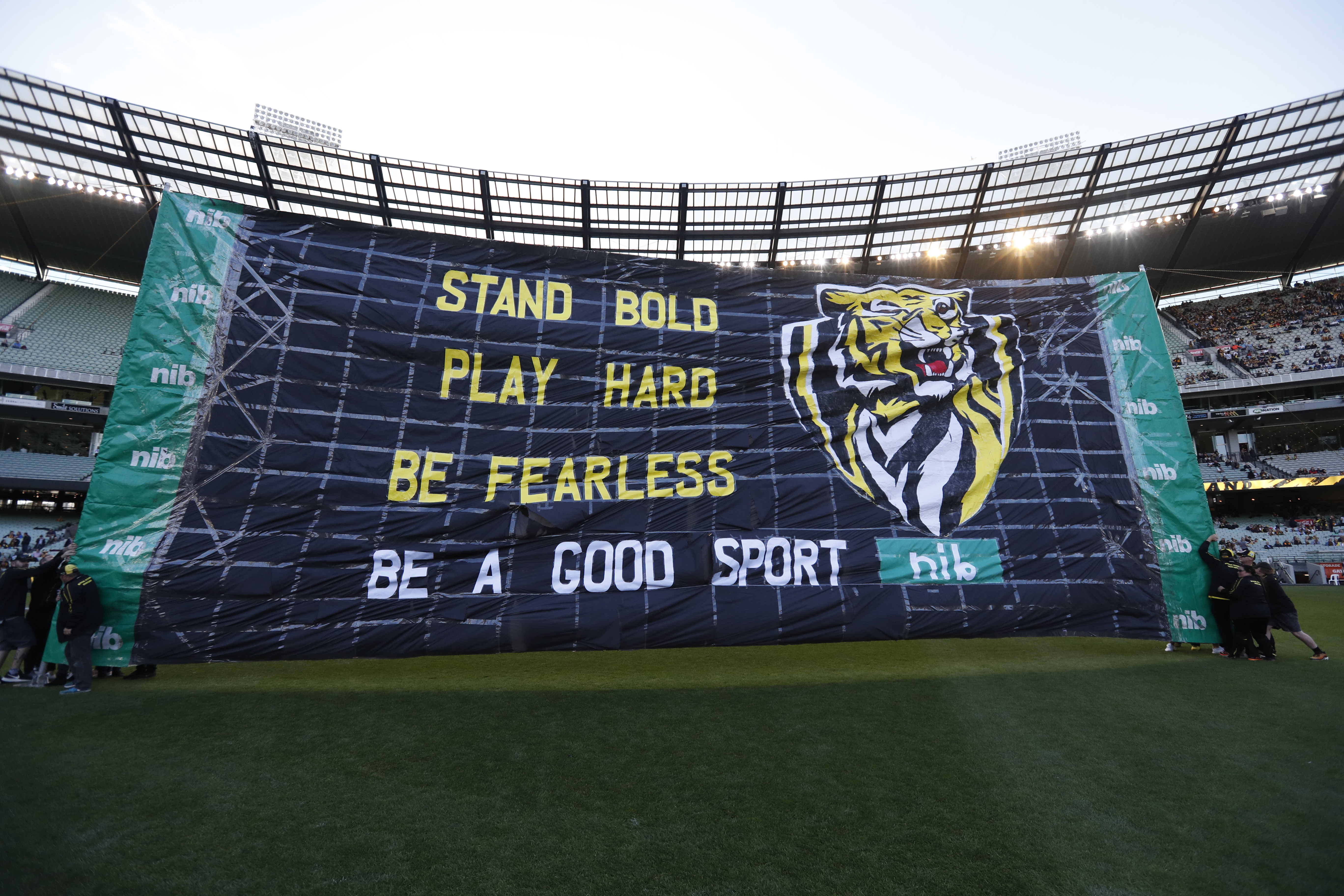 A large banner that reads 'Stand Bold, Play Hard, Be Fearless, Be a Good Sports' displayed in a football stadium