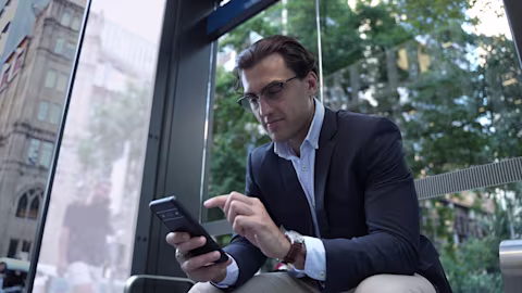 Man in glasses sitting outdoors and looking at his phone Man in glasses sitting outdoors and looking at his phone