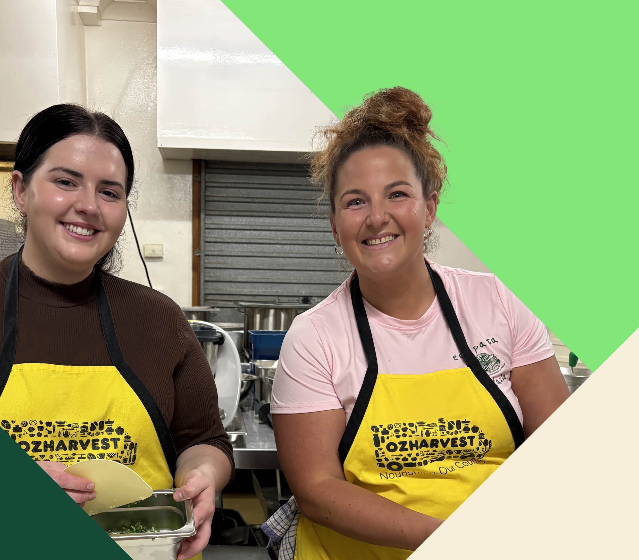 Two women wearing yellow OzHarvest aprons smiling and cooking in a kitchen