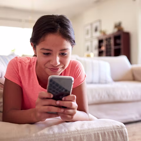 Young teen girl in peach top on couch smiling at phone Young teen girl in peach top on couch smiling at phone