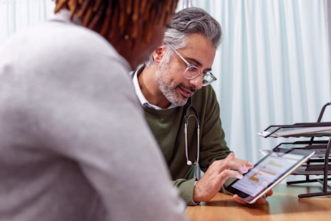 A male doctor speaks to a patient while showing his iPad screen A male doctor speaks to a patient while showing his iPad screen