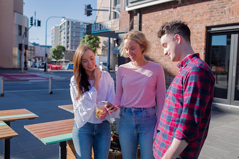 Three people standing in the street looking at a phone Three people standing in the street looking at a phone