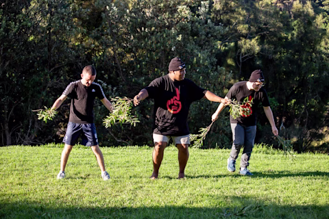 Three young men outside on the grass performing an indigenous ceremony Three young men outside on the grass performing an indigenous ceremony