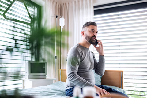 A man sits on his hospital bed speaking on the phone A man sits on his hospital bed speaking on the phone