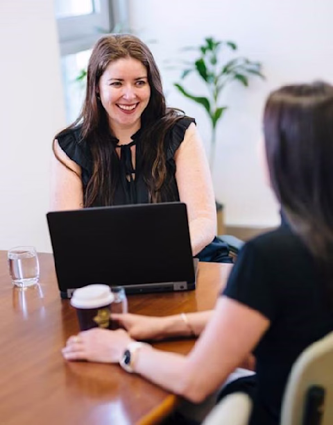 Claire Holland sitting at a desk speaking with a colleague Claire Holland sitting at a desk speaking with a colleague