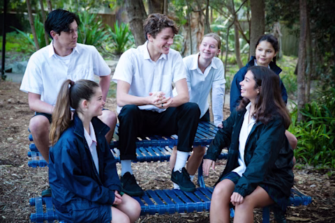 Group of teenagers sitting on and around an outdoor picnic table, laughing and talking to each other. Group of teenagers sitting on and around an outdoor picnic table, laughing and talking to each other.