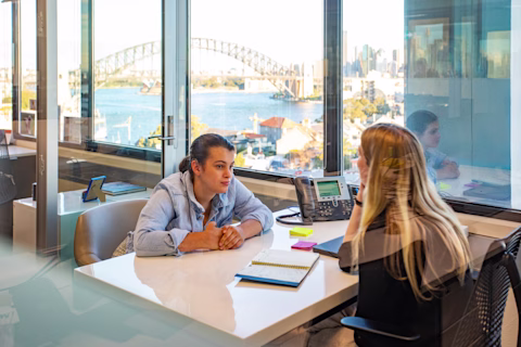 Two people sitting across a desk from one another. Two people sitting across a desk from one another.