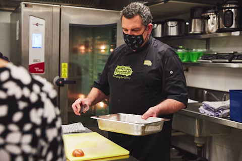 OzHarvest head chef in the kitchen holding a tray OzHarvest head chef in the kitchen holding a tray