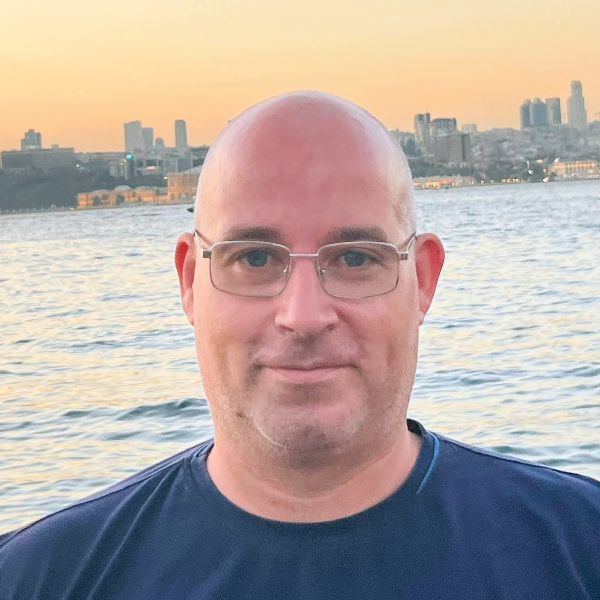 Front facial photo of Atanas Atanasov smiling and standing at the beach on the Black sea wearing sunglasses and darkblue t-shirt.