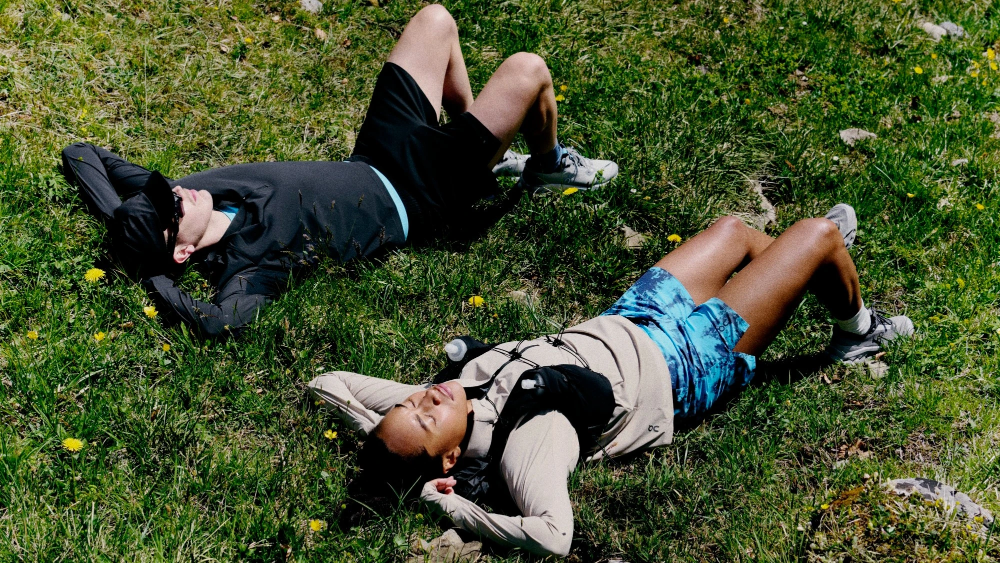 Zwei Läufer*innen liegen mit geschlossenen Augen auf einer Wiese. 