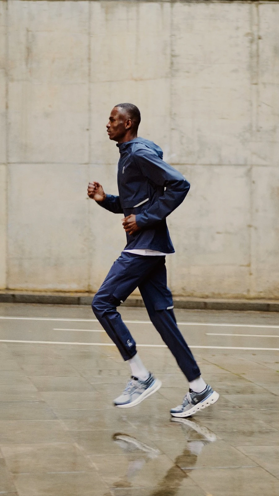 Two runners wearing On outerwear running on a wet street.