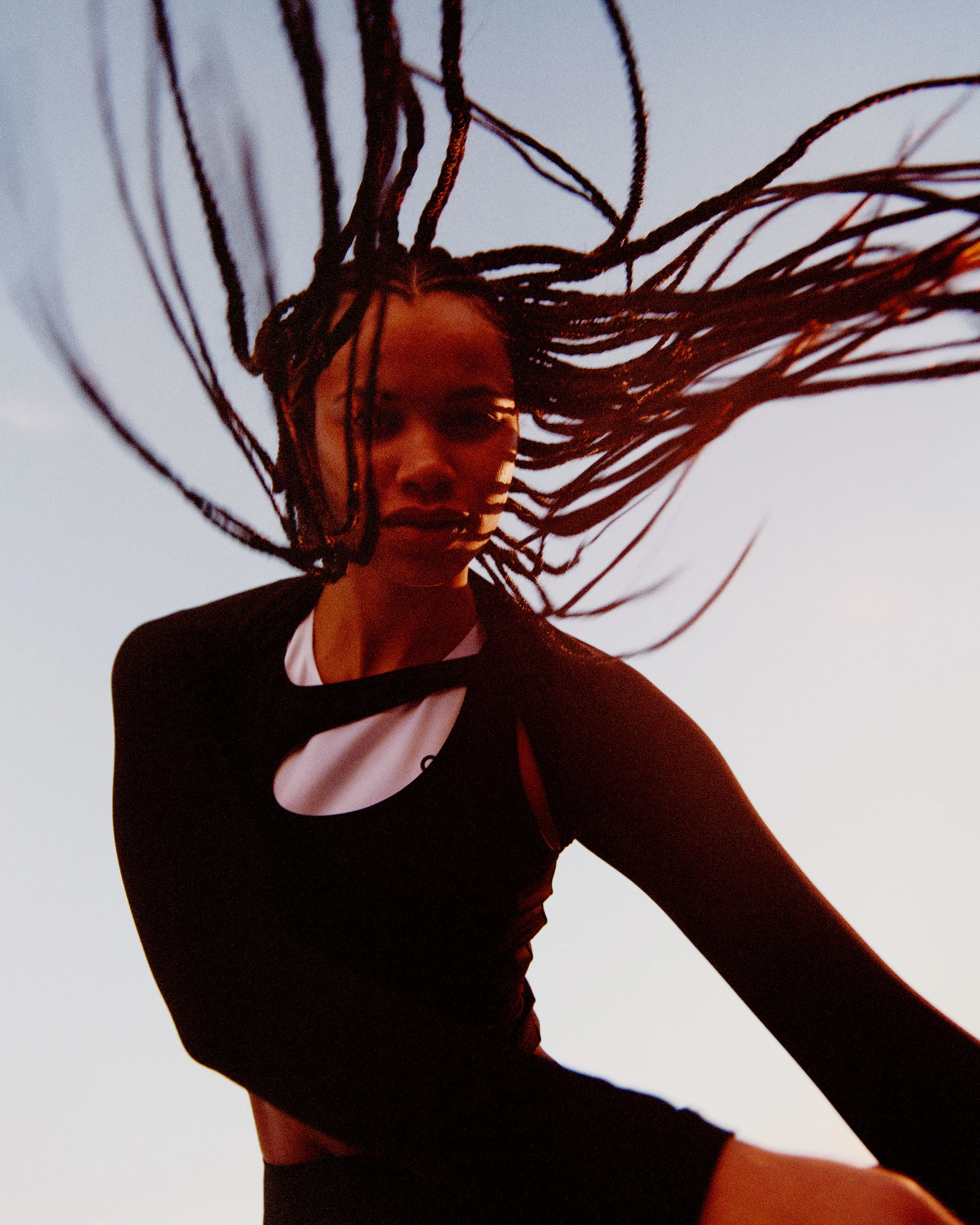 A female athlete moving dynamically with braided hair in motion, wearing On performance gear.