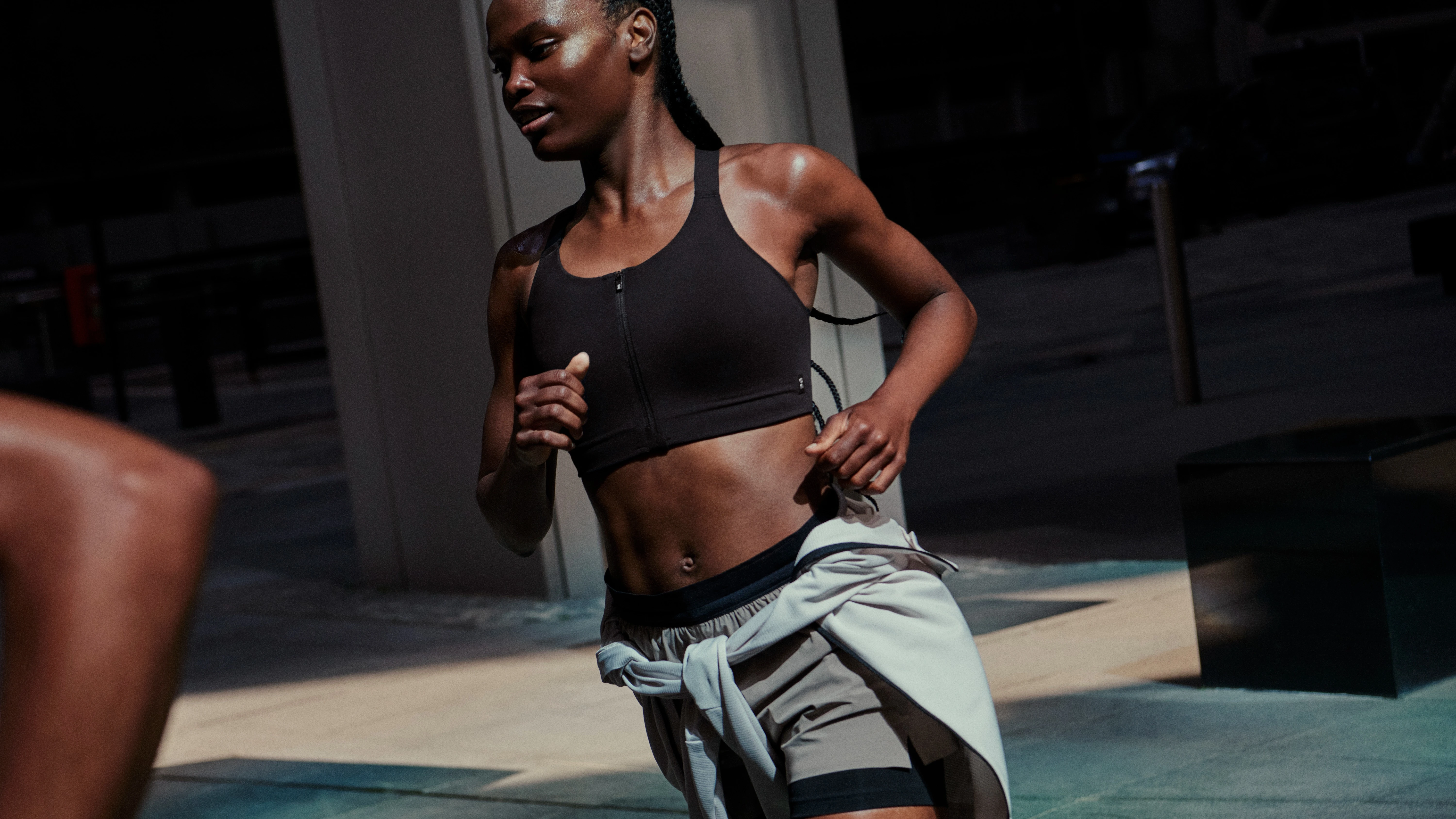 A woman running in a sports bra and shorts with a sweater wrapped around her waist. 