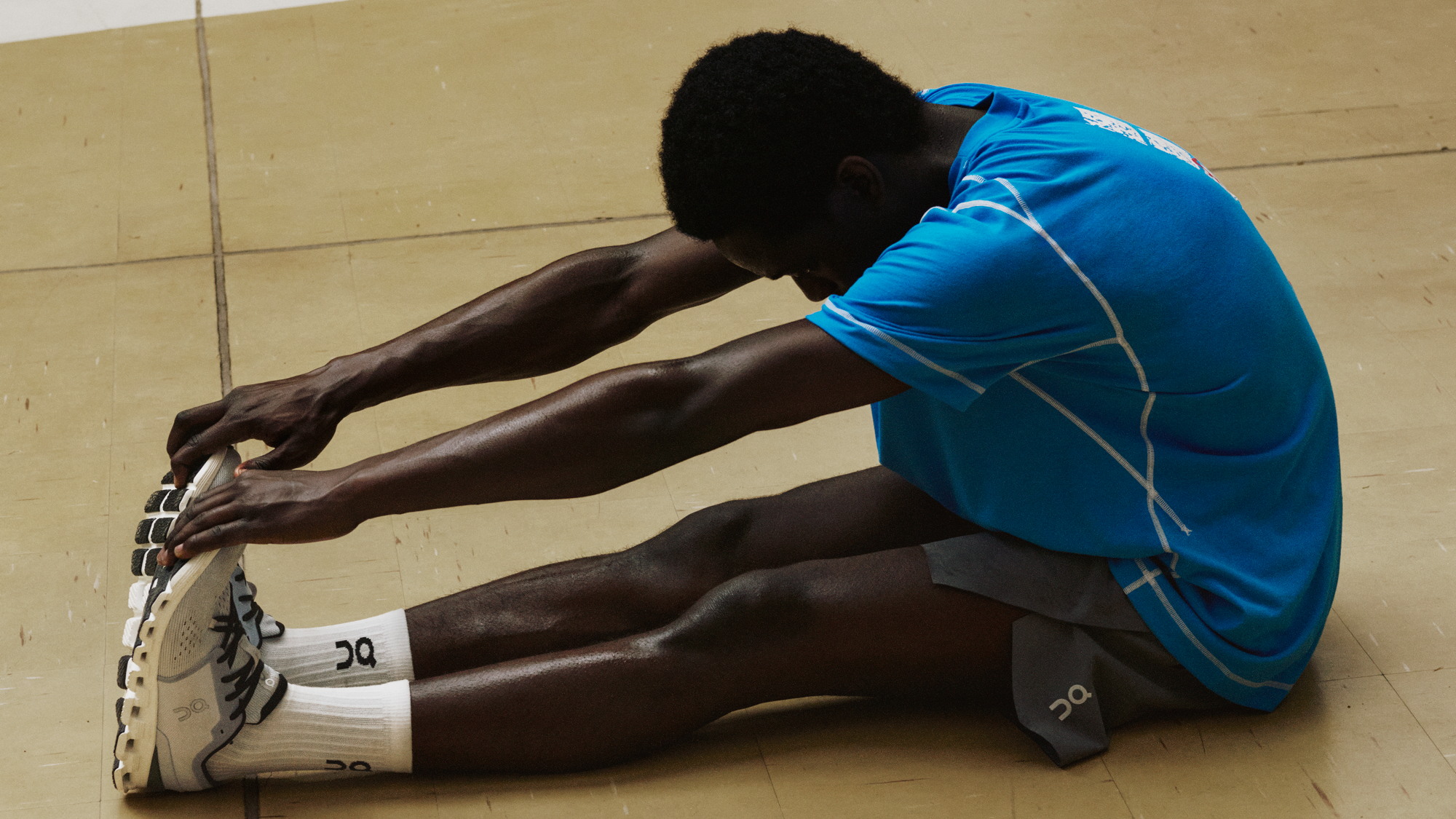 Man doing a seated forward fold stretch while wearing On performance gear and shoes.