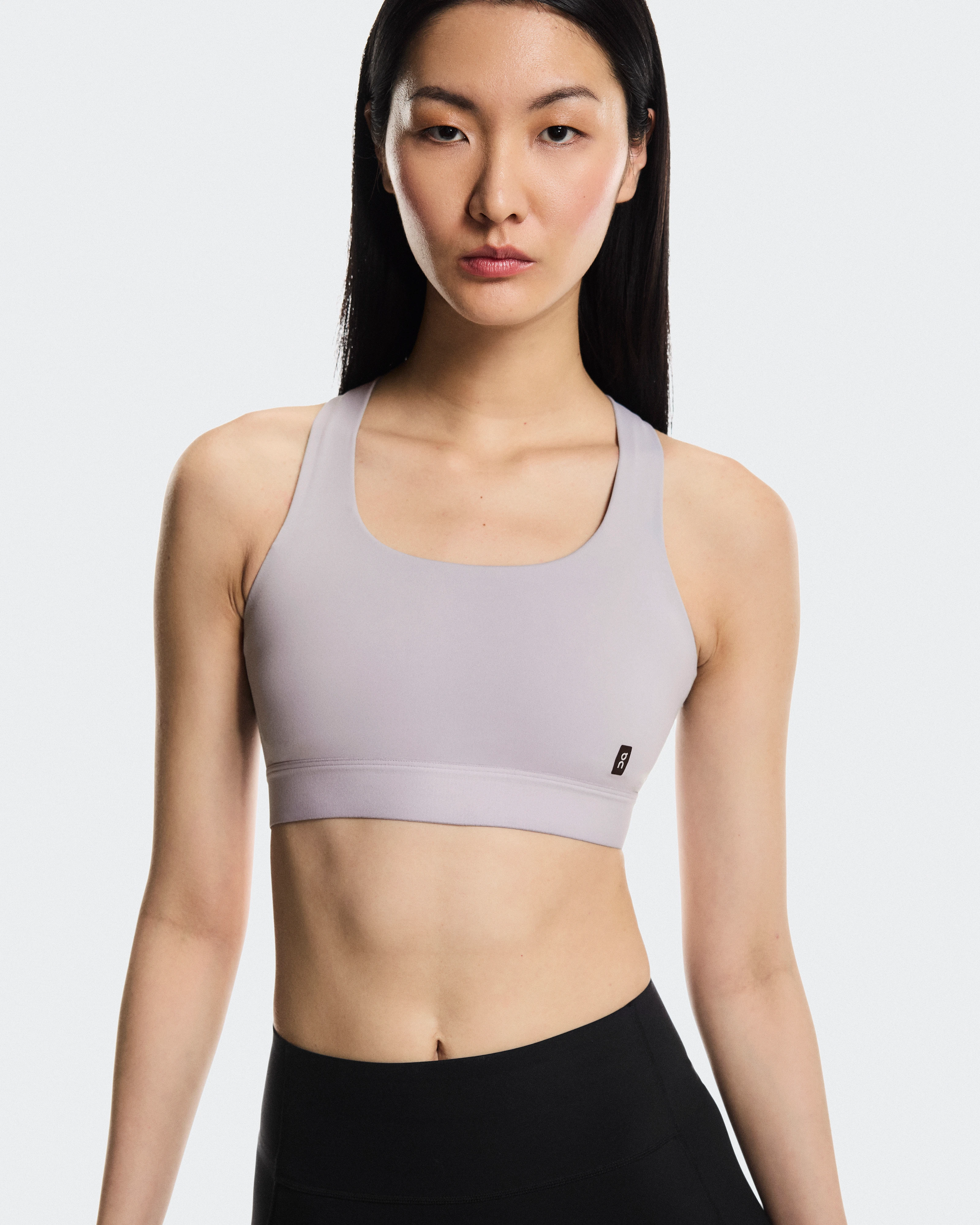 A woman wearing an On sports bra and leggings, looking seriously at the camera.