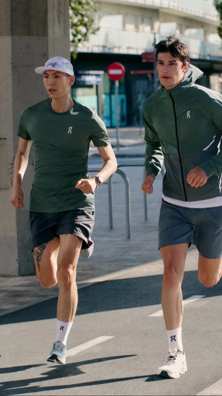 Two runners in On gear running towards the camera on a city pathway. 