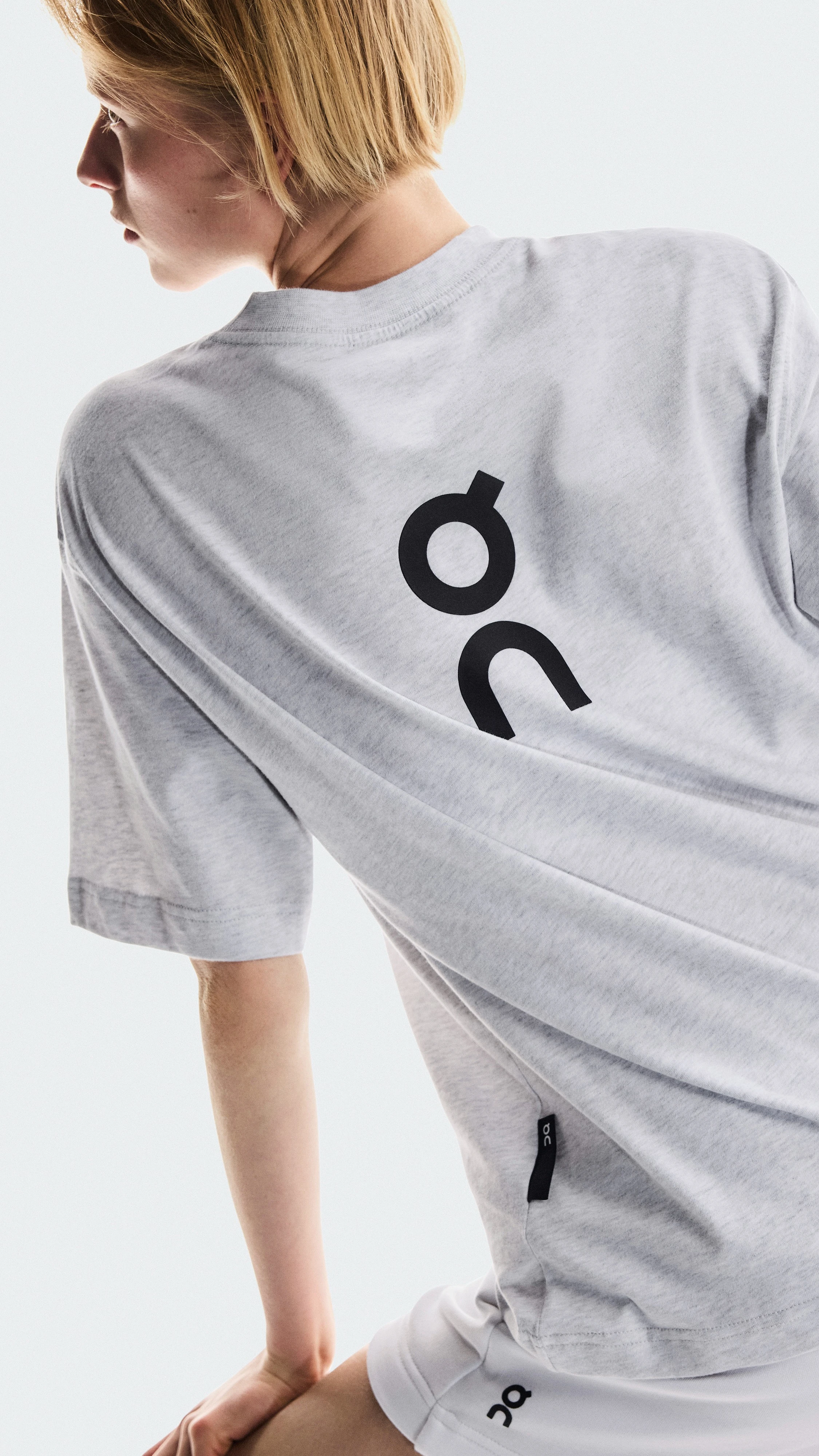 A medium shot of a person from the back in a grey "On" t-shirt and white shorts, against a white background.