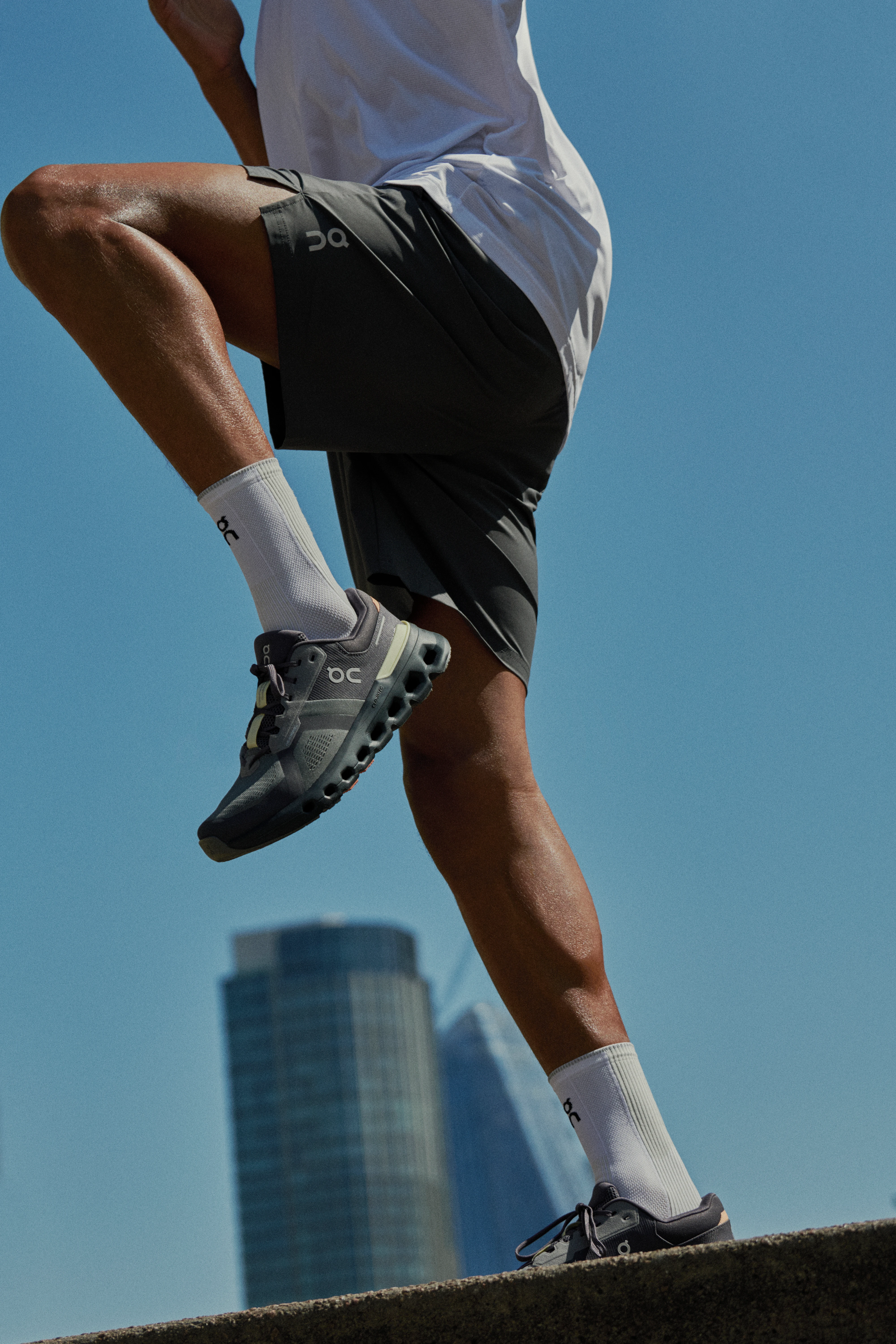 A runner drives their legs up in high-knees, a skyscraper in the background.