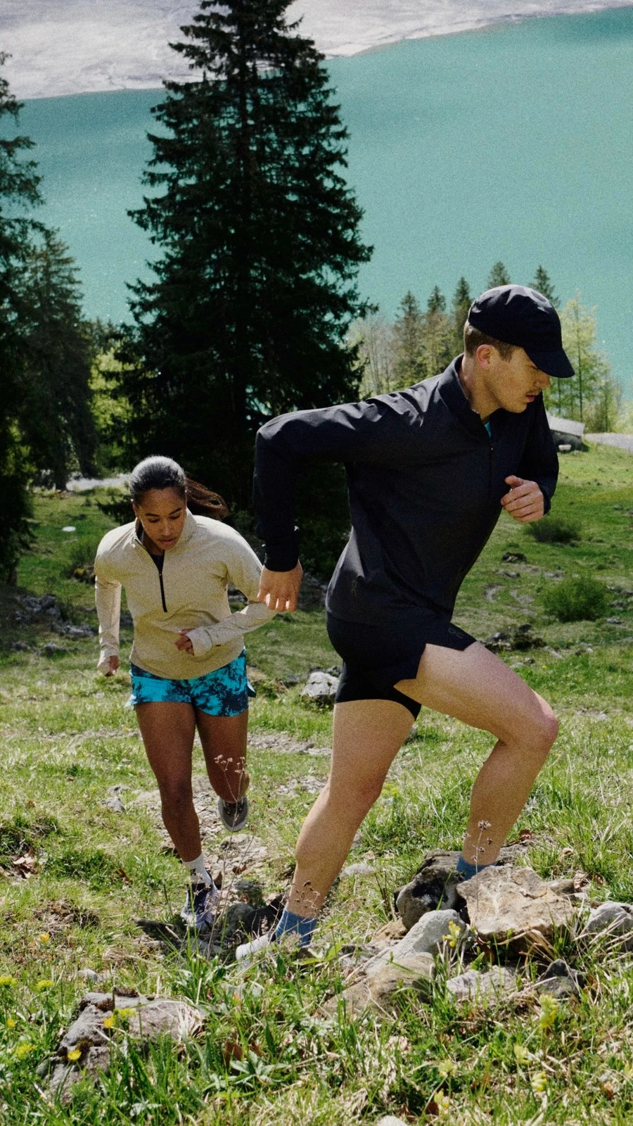 Zwei Läufer*innen laufen eine Bergwiese hoch.
