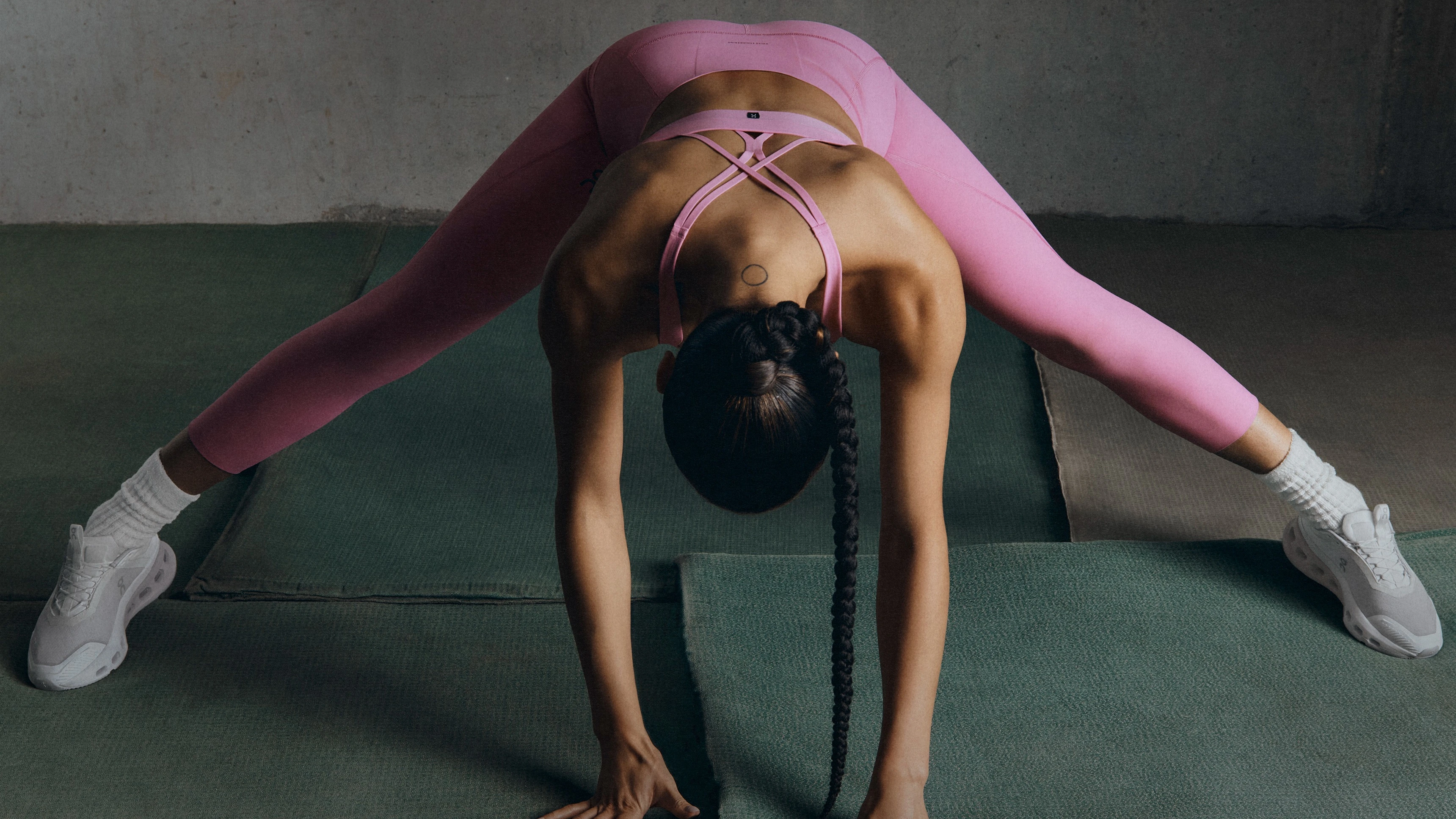 Una mujer hace yoga con zapatillas de tenis, un sujetador deportivo y mallas rosas. 