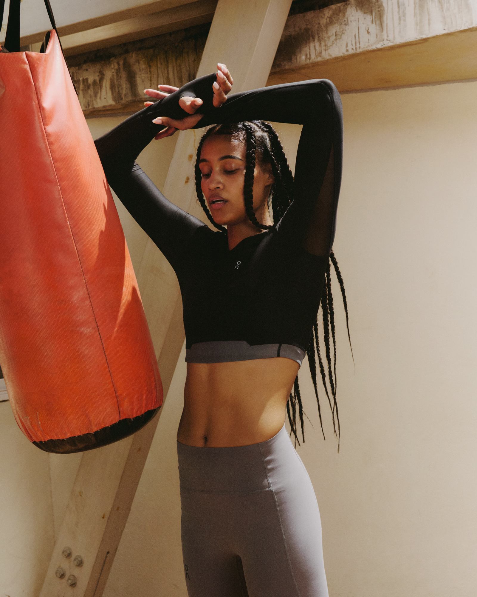 A woman standing with her hands over her head next to an orange punching bag. 