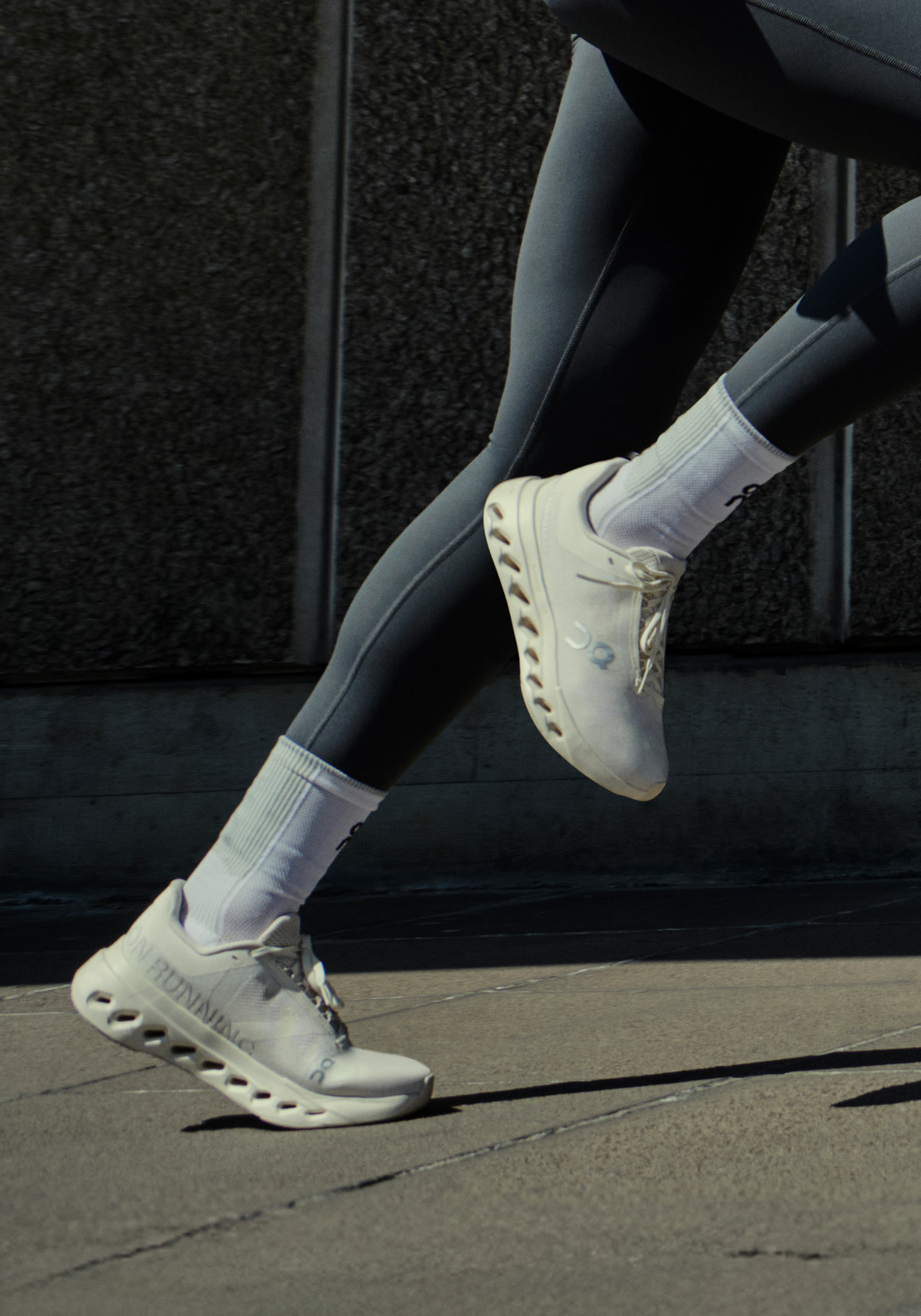 Close-up of a runner’s legs in On shoes and tights mid-stride on pavement.