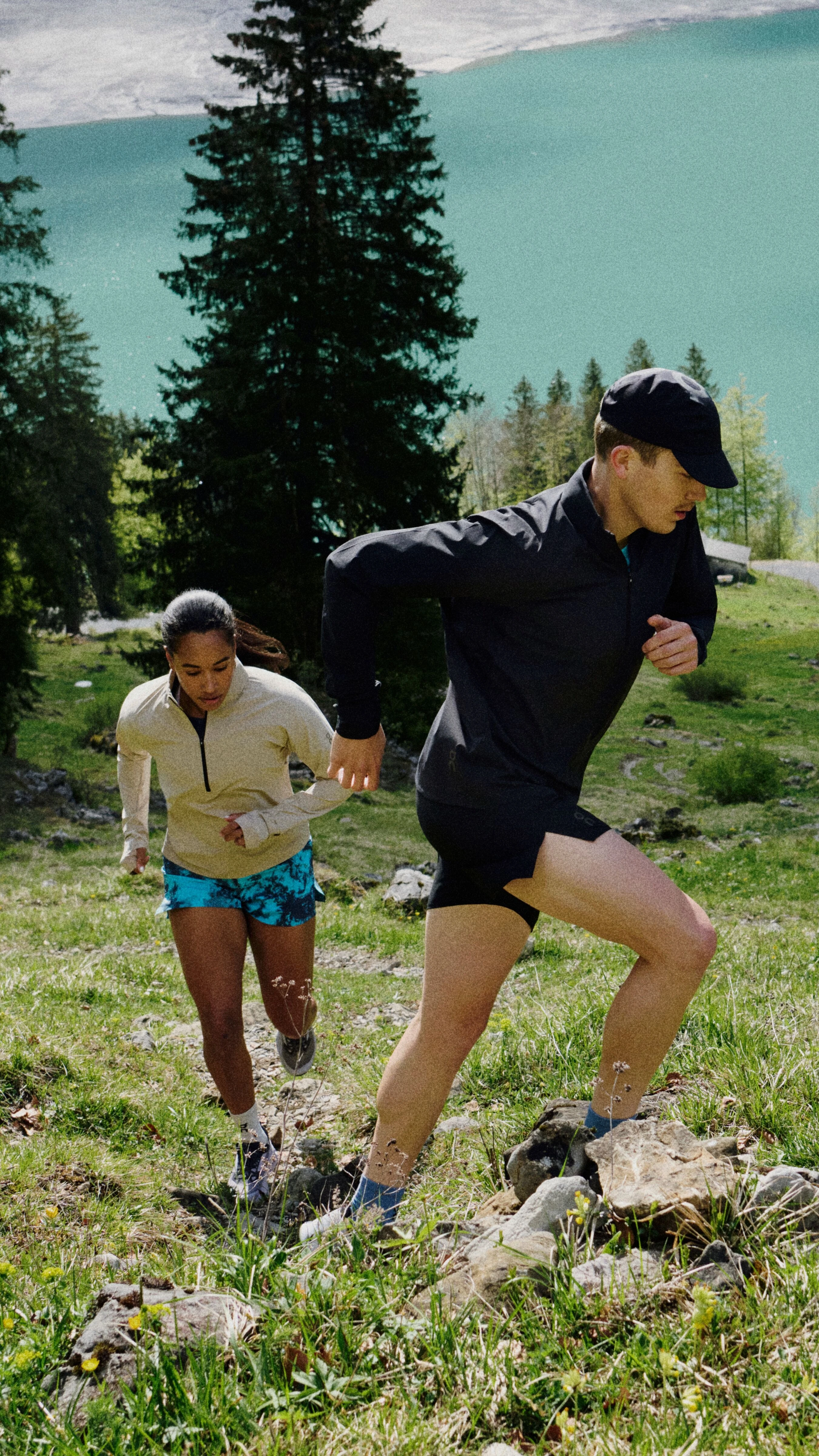 Two hikers in On gear hiking up a grassy mountainside.