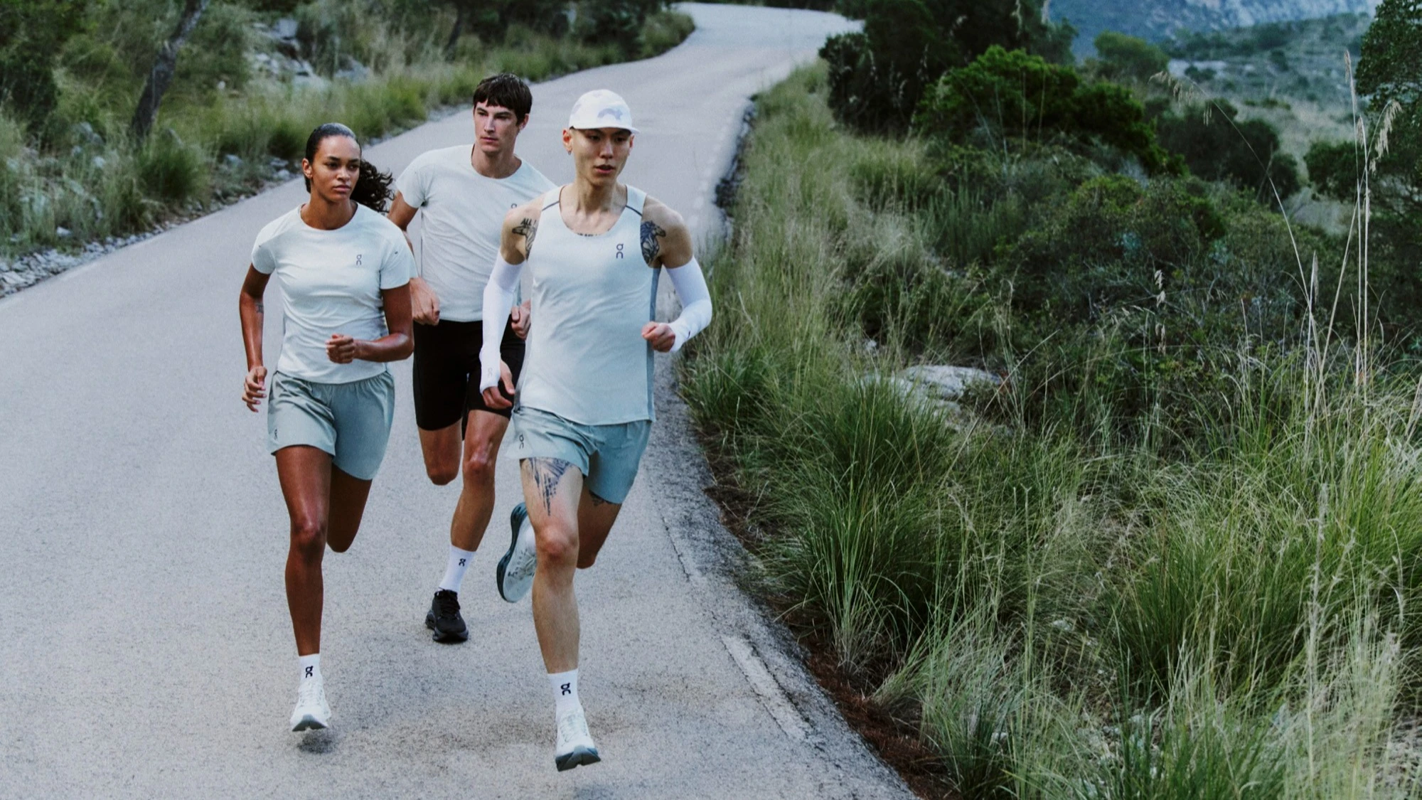 Three runners in On gear on a paved mountain road.