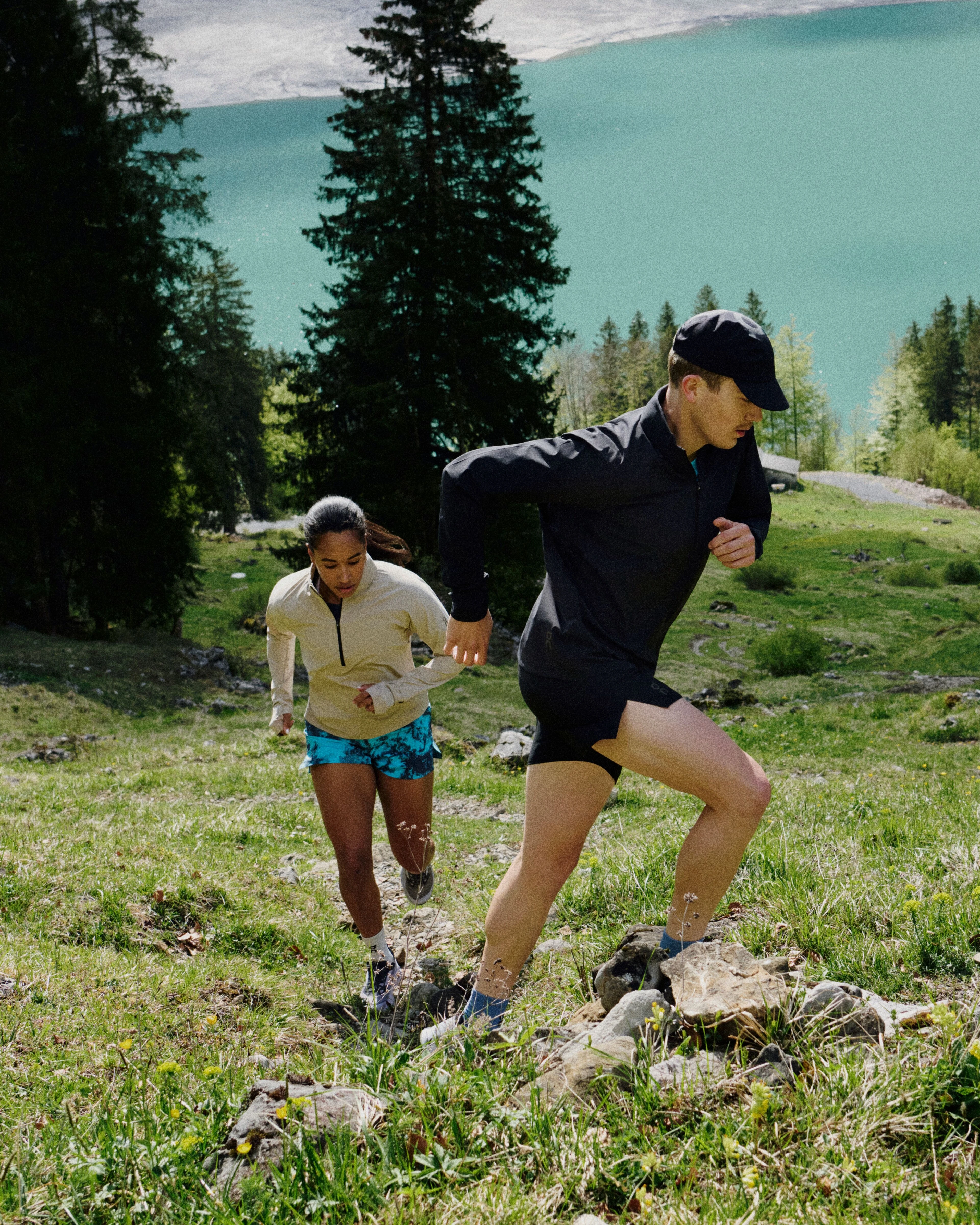 Two hikers in On gear hiking up a grassy mountainside. 