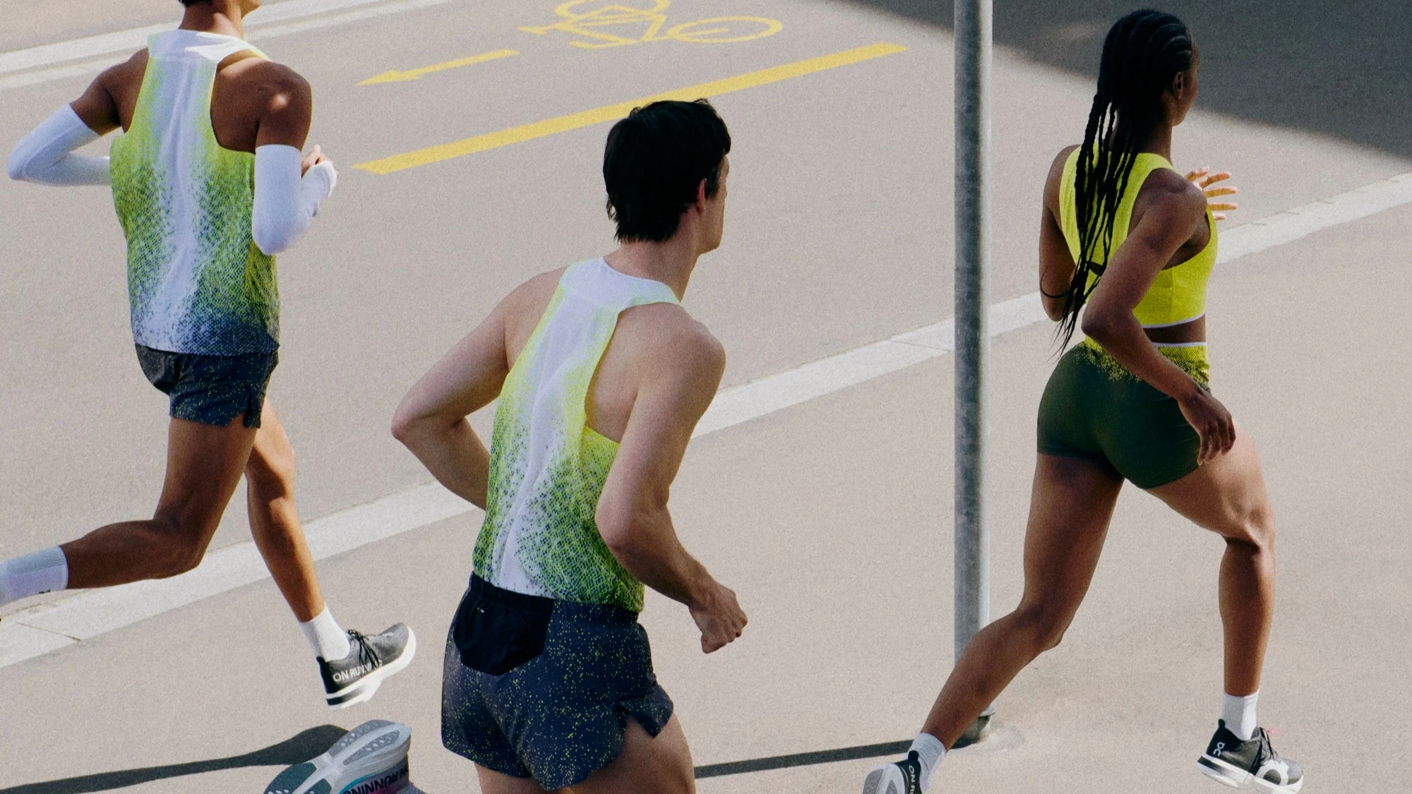 Three runners in On apparel mid-stride on pavement.