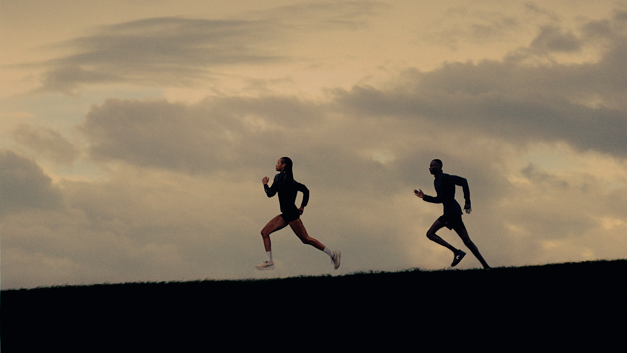 Due atleti che corrono su una collina all’aperto indossando le scarpe da corsa On.