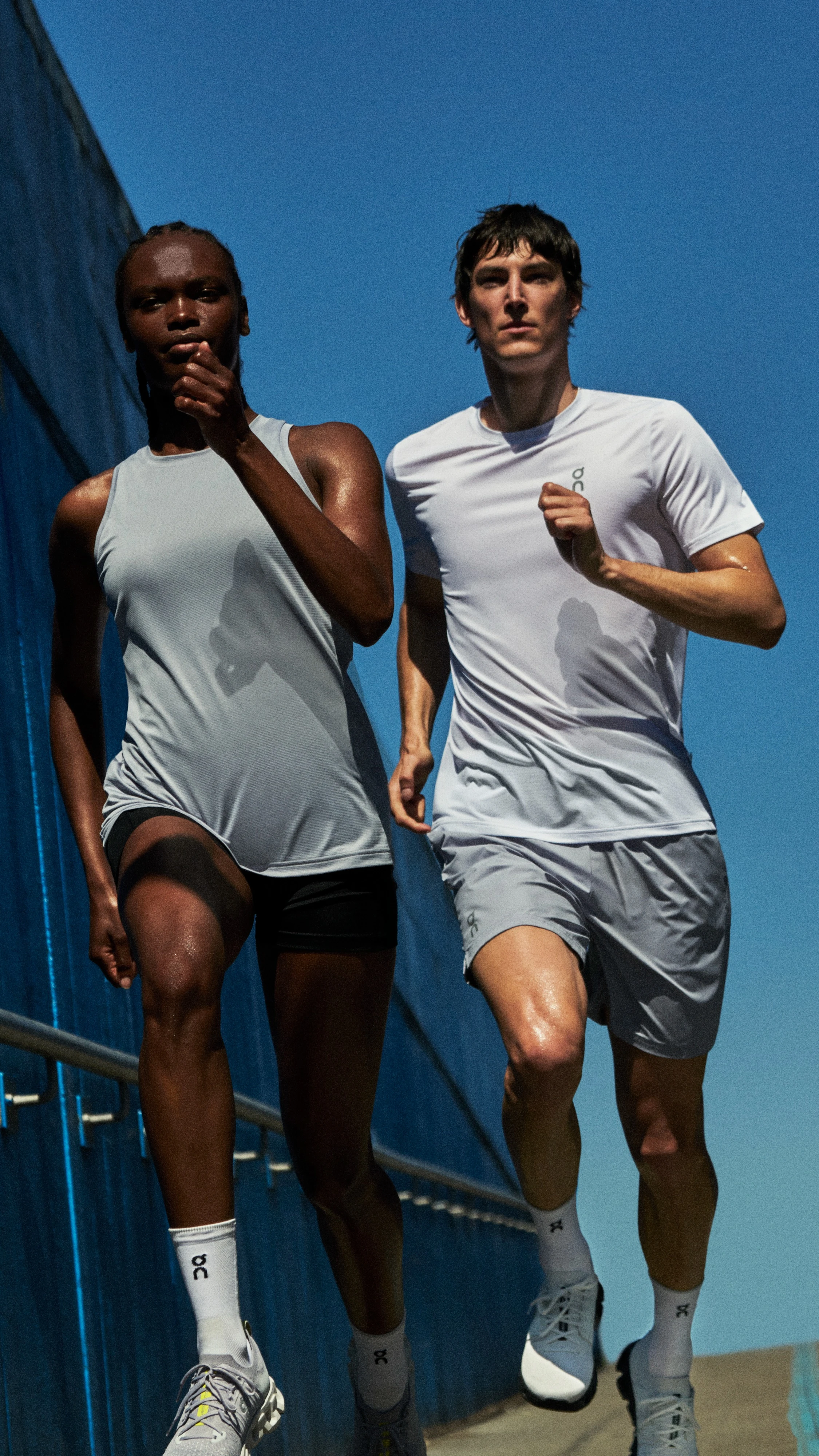 Two men in On running gear run side-by-side across a bridge.