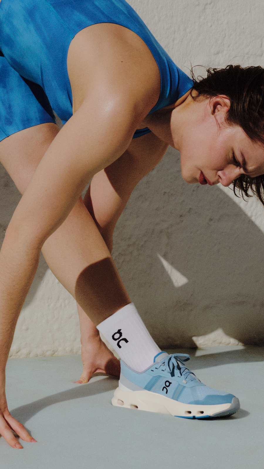 Person in athletic wear doing a morning stretch while wearing On running shoes and socks.