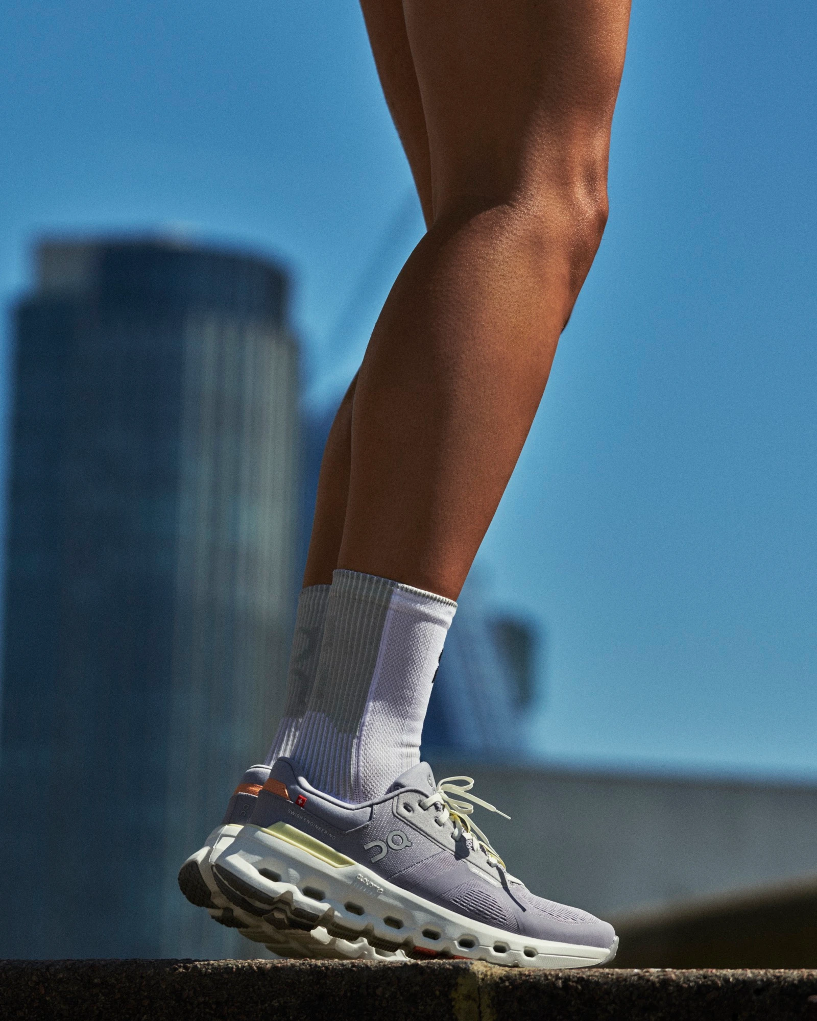 A person’s legs with On running shoes and a city skyline in the background.