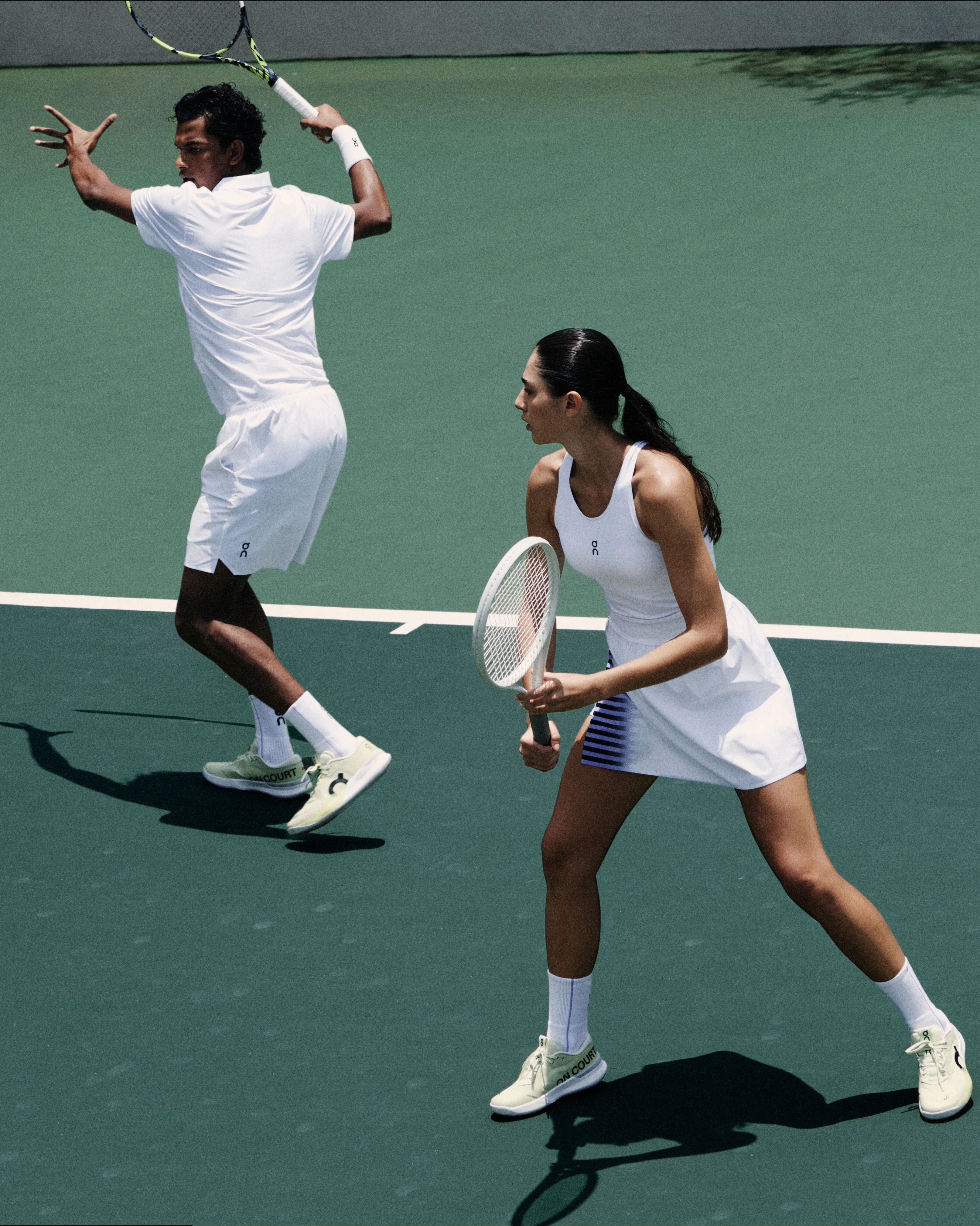 Tennis players in On tennis whites, mid swing.
