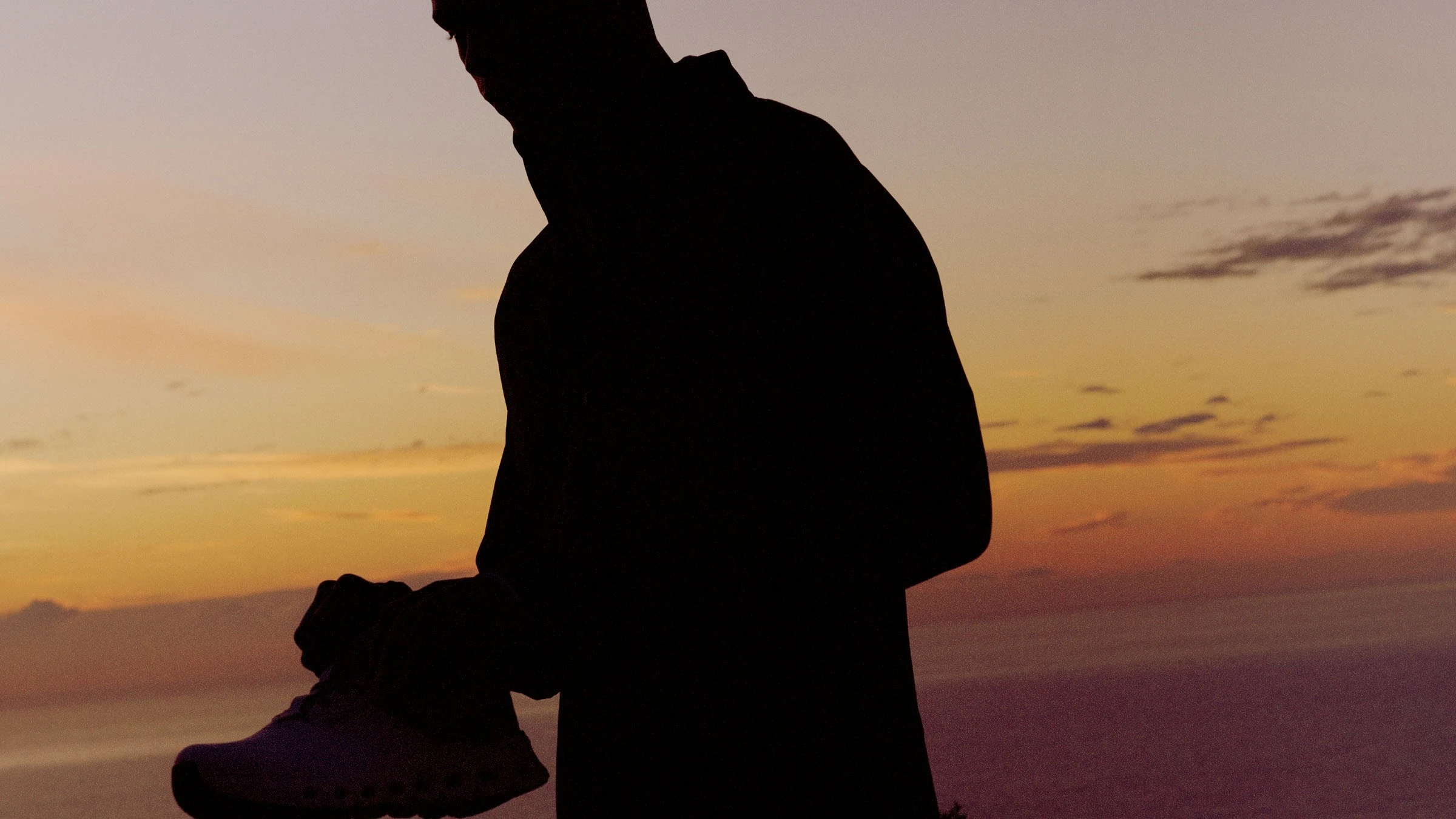 Un uomo si mette le scarpe prima di una corsa al tramonto.