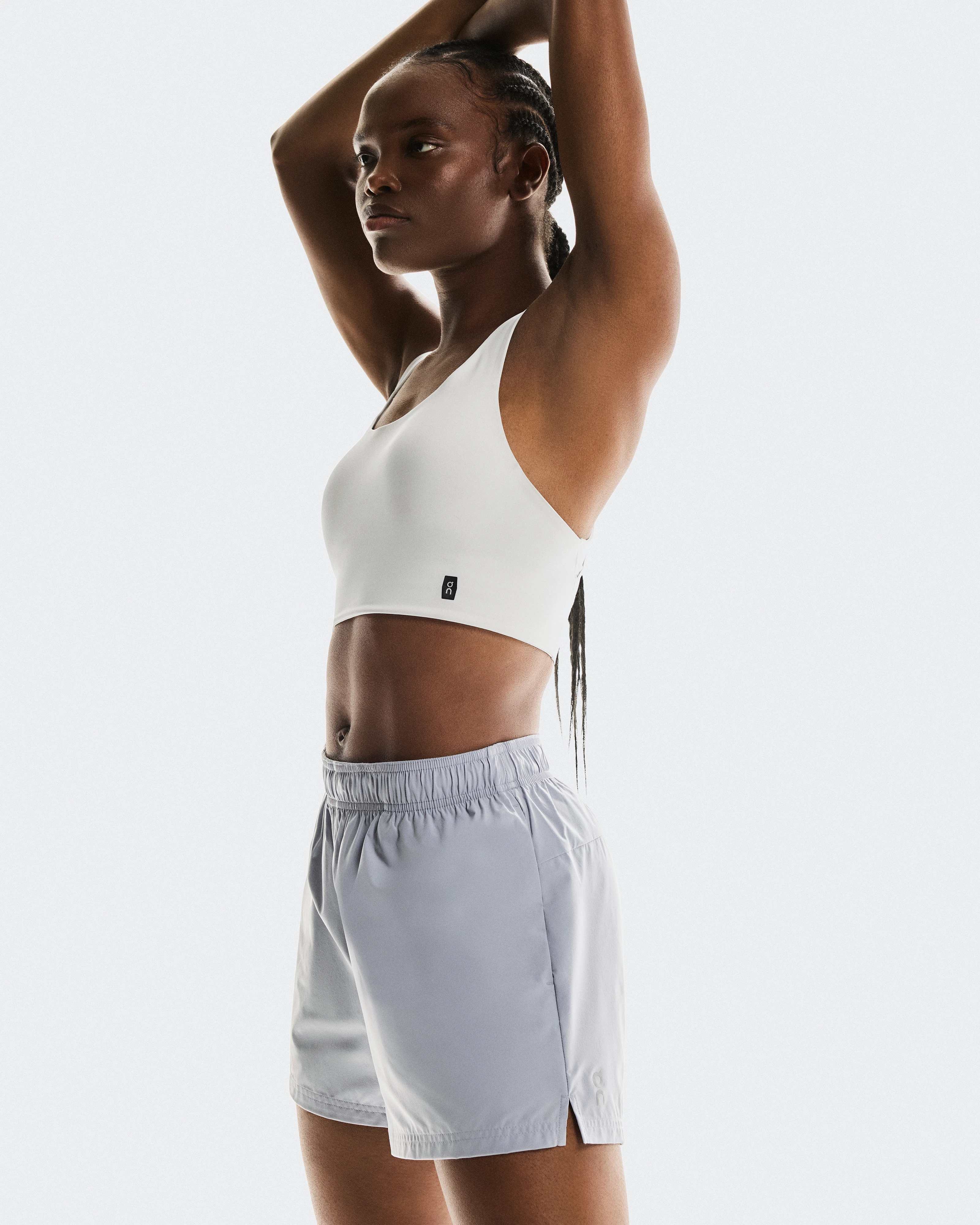 A female athlete stretching her shoulders, wearing a white sports bra and On running shorts.
