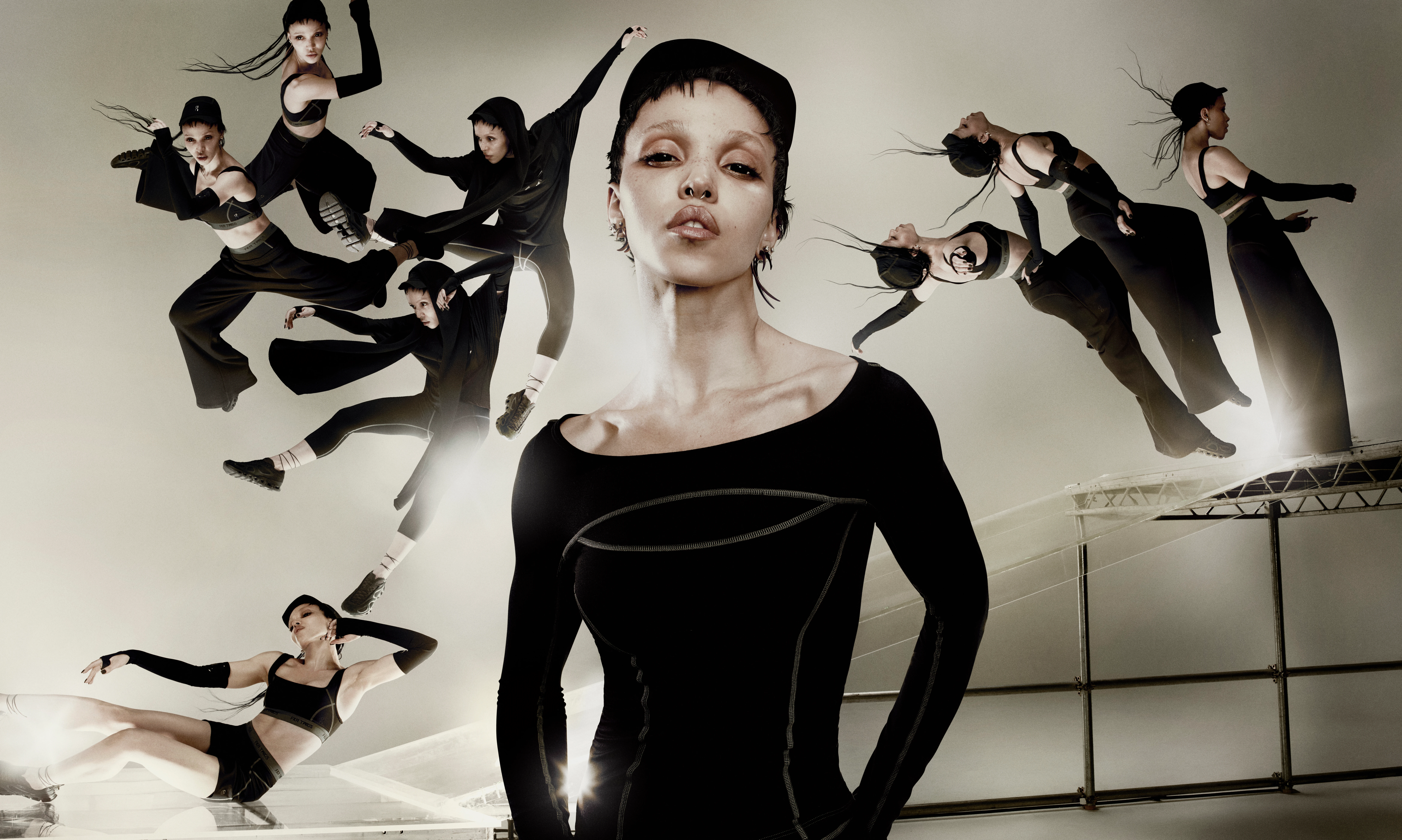 A focused FKA Twigs in a black long-sleeved top from her On capsule collection is surrounded by multiple blurred, moving images of herself against a beige architectural backdrop.