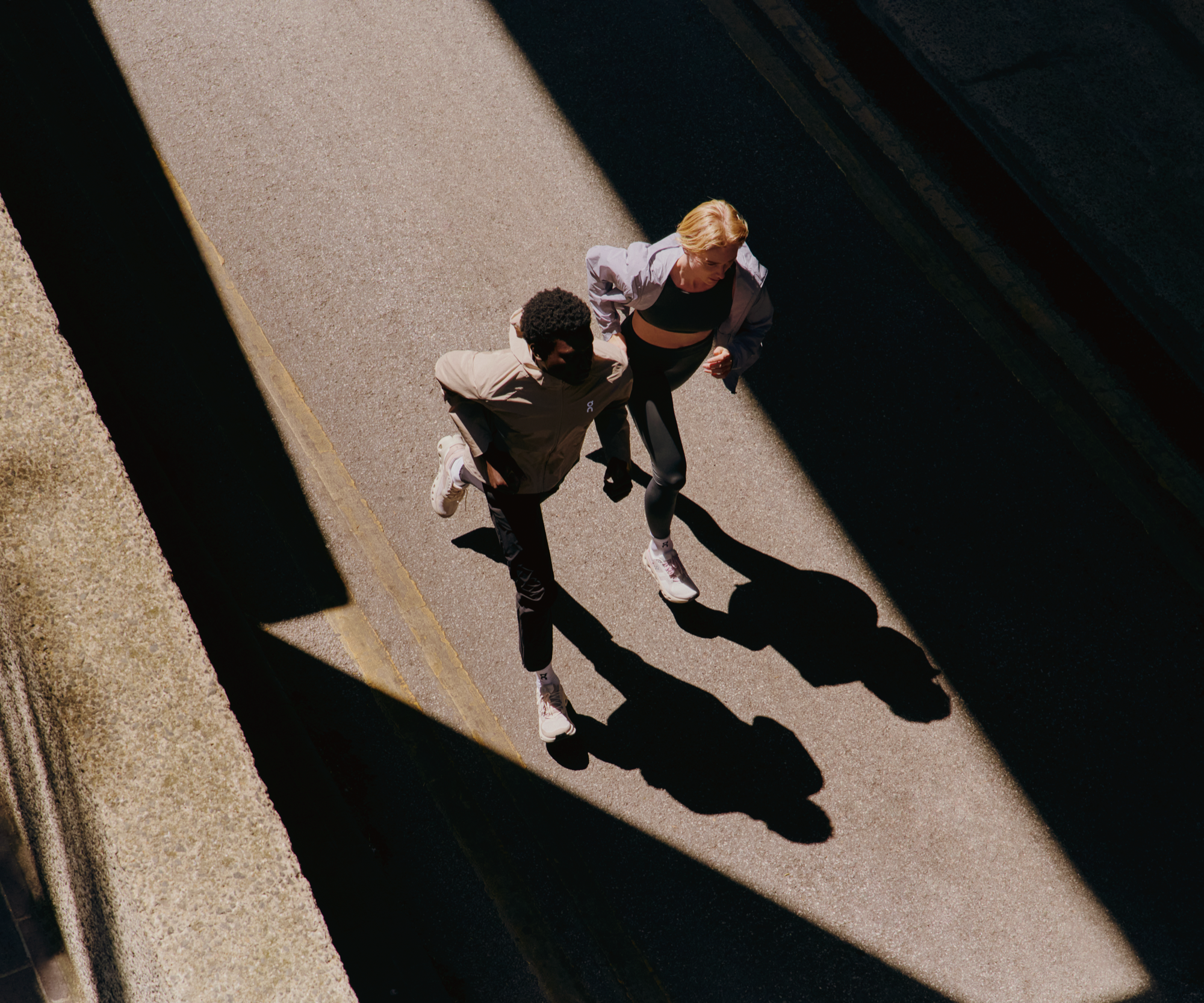 Dos runners corren por la calle con zapatillas y sudaderas de rendimiento con capucha de On.