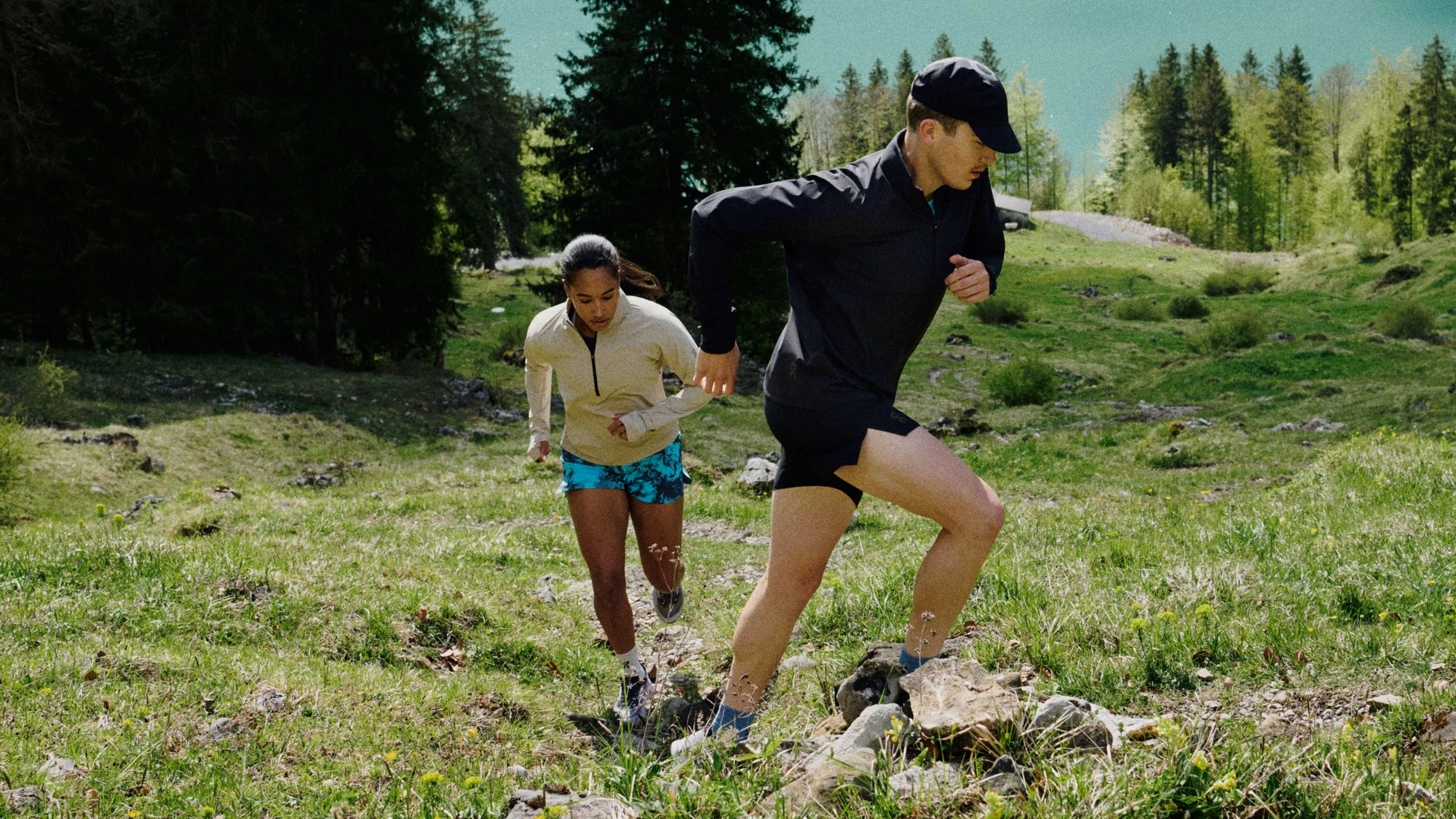 Zwei Läufer*innen laufen eine Bergwiese hoch.