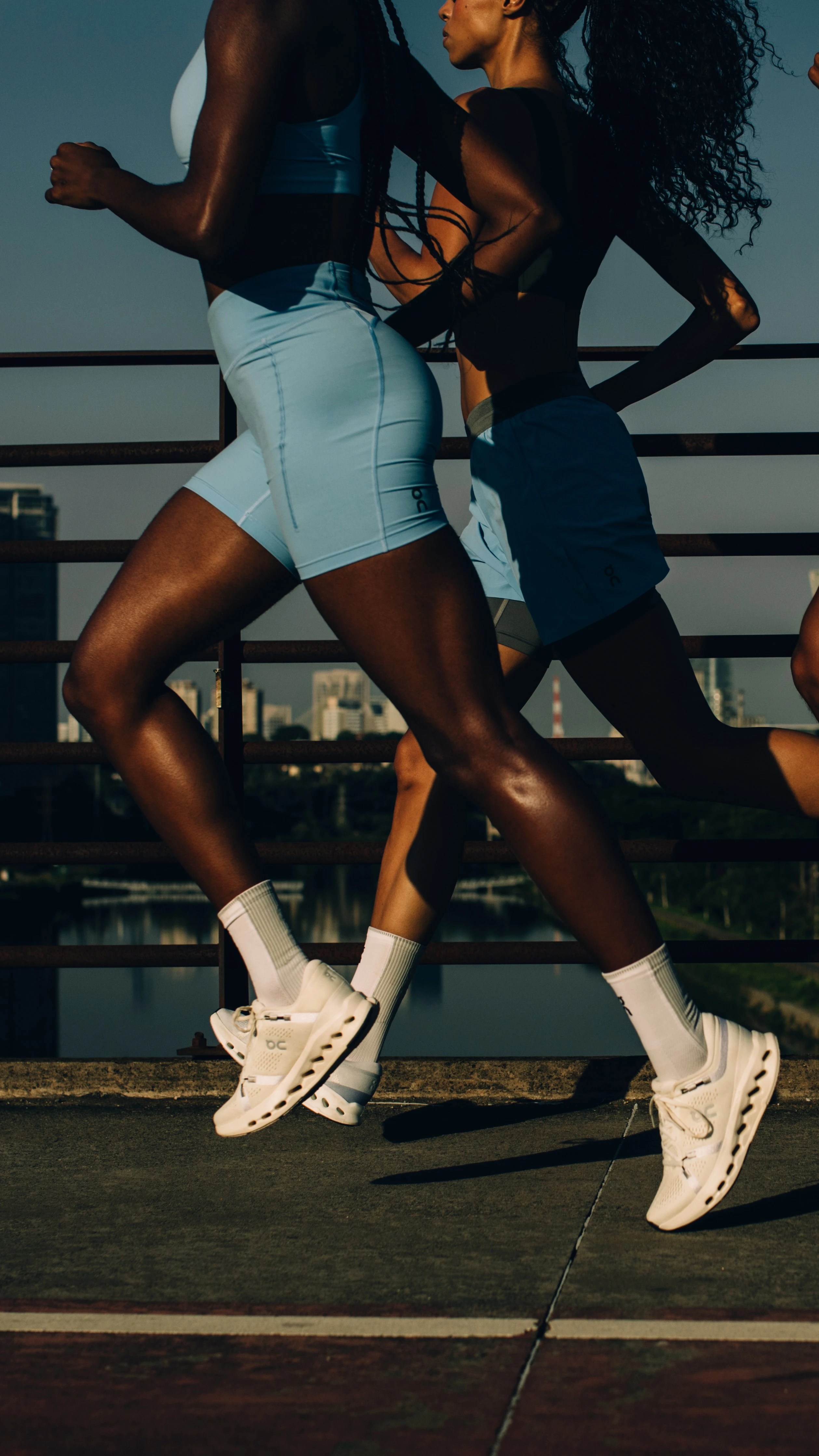 Three runners in On gear with their heads out of frame, running across a bridge in the city. 