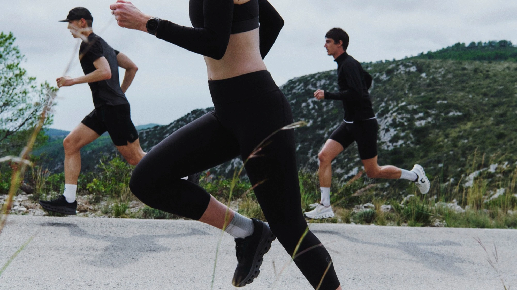 Three runners in On apparel running on a mountain road.