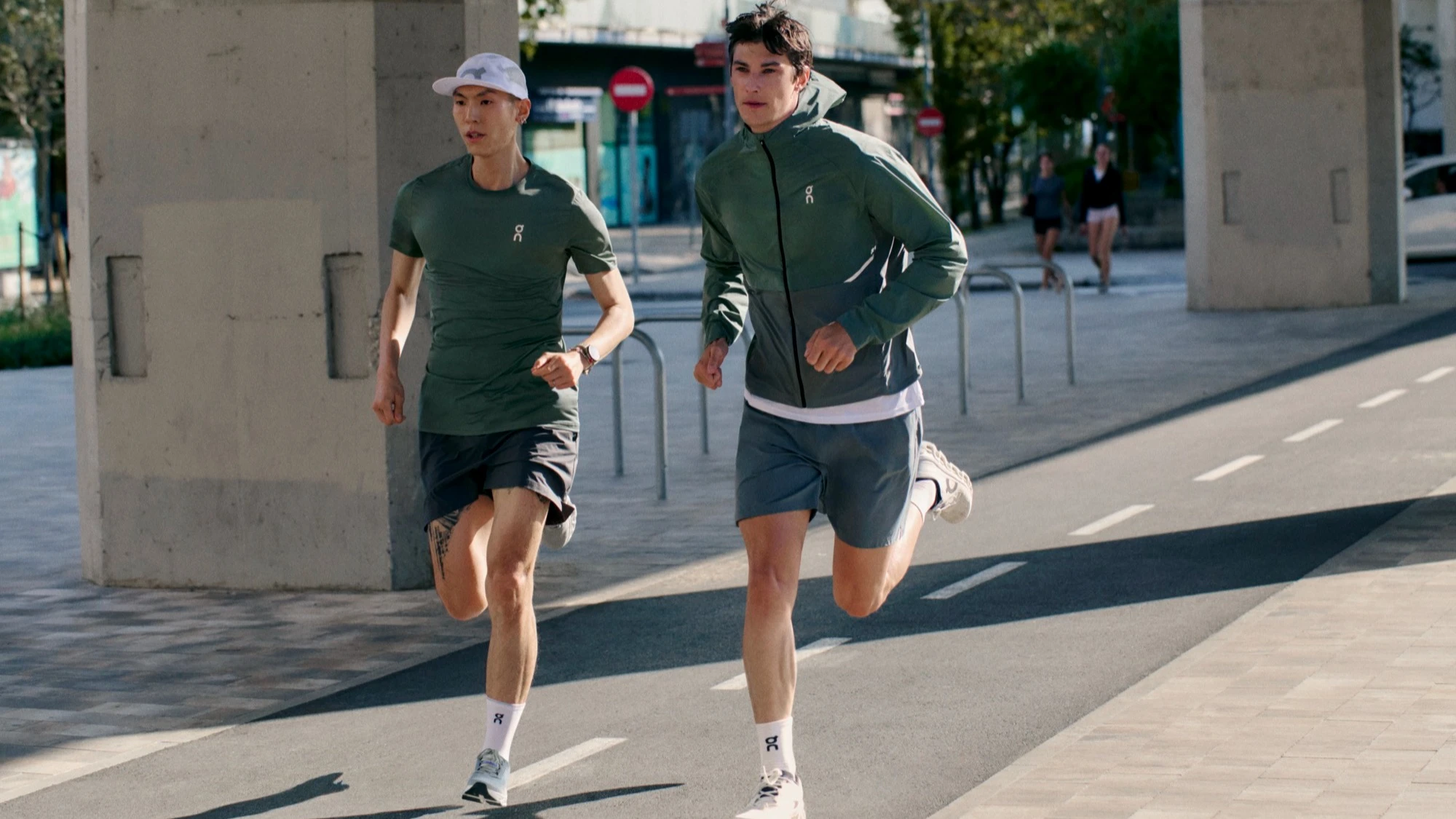 Two runners in On gear running towards the camera on a city pathway. 