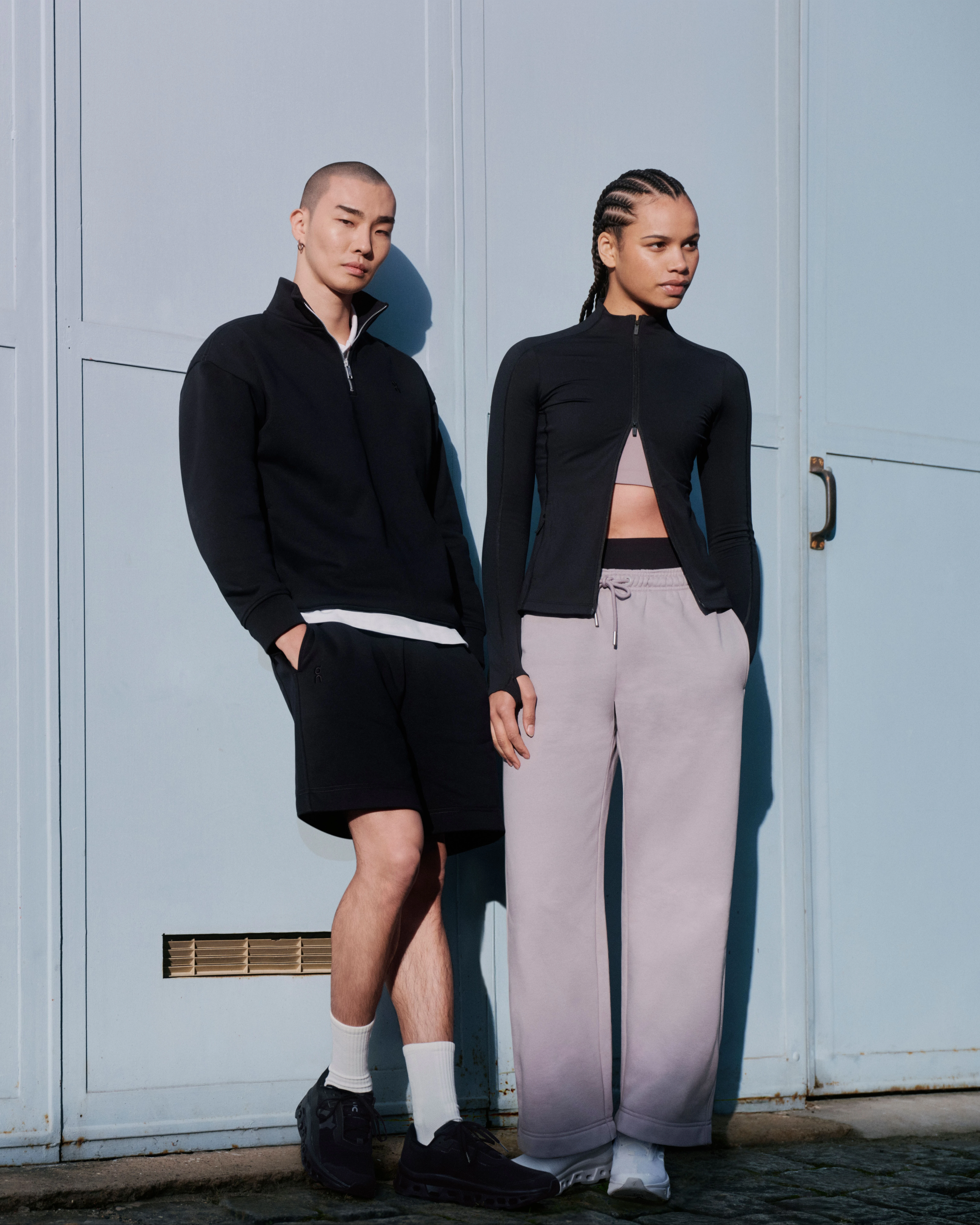 Dos personas con ropa On de estilo urbano posando contra una pared.