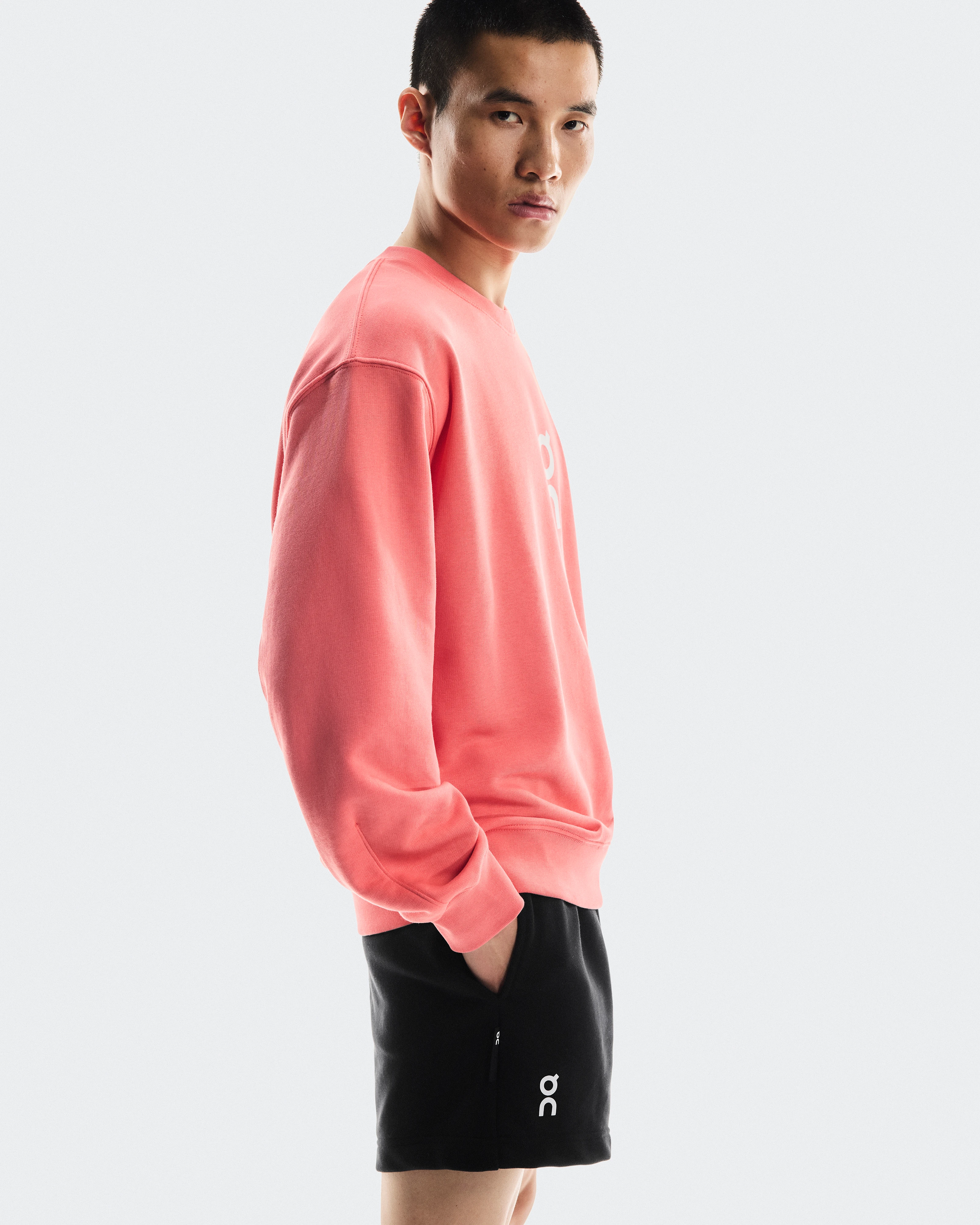 A male athlete looking serious with hands in his pockets, wearing On shorts and a crewneck sweatshirt .