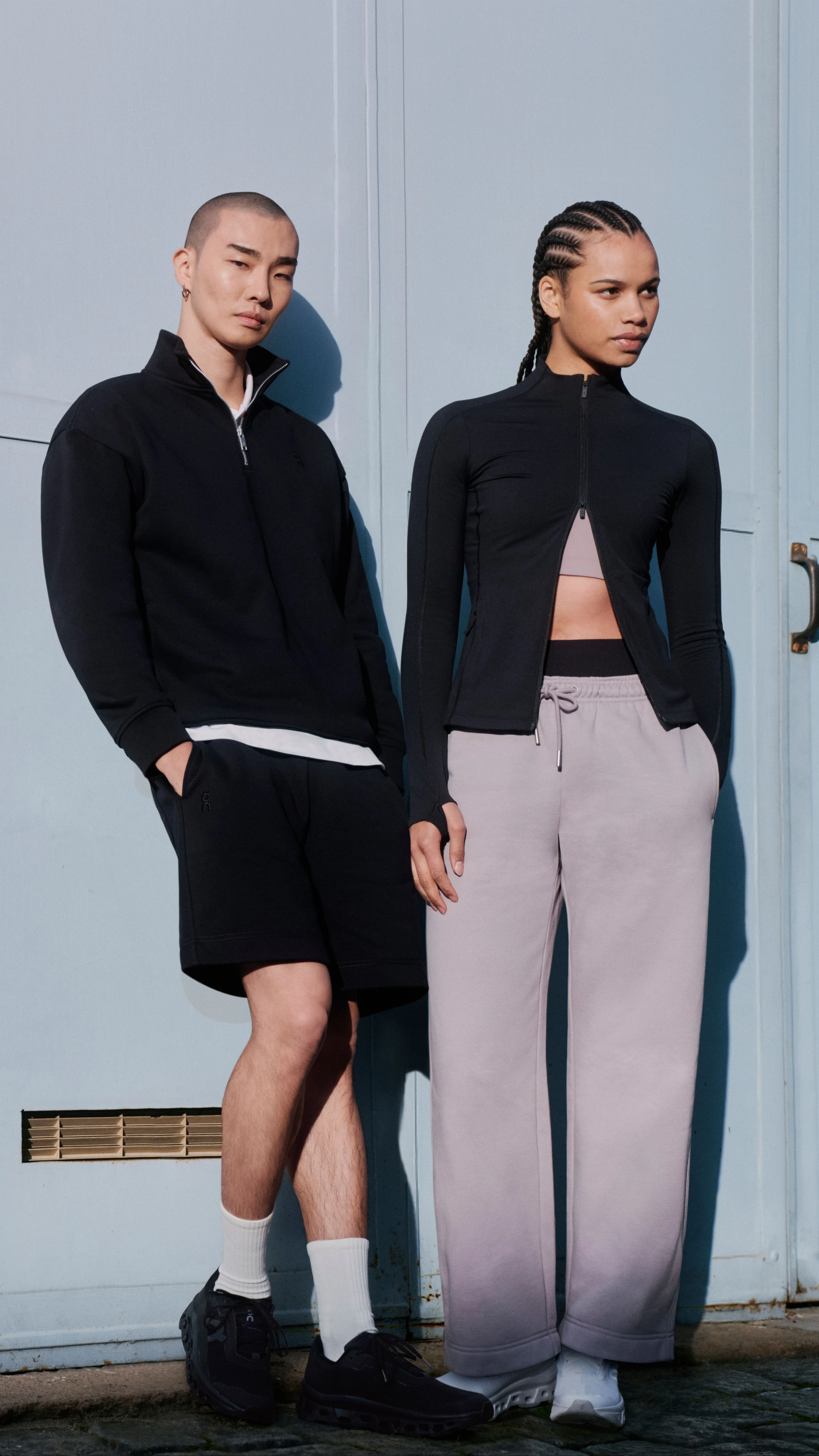 Zwei Menschen in On Streetwear lehnen gegen eine Wand.
