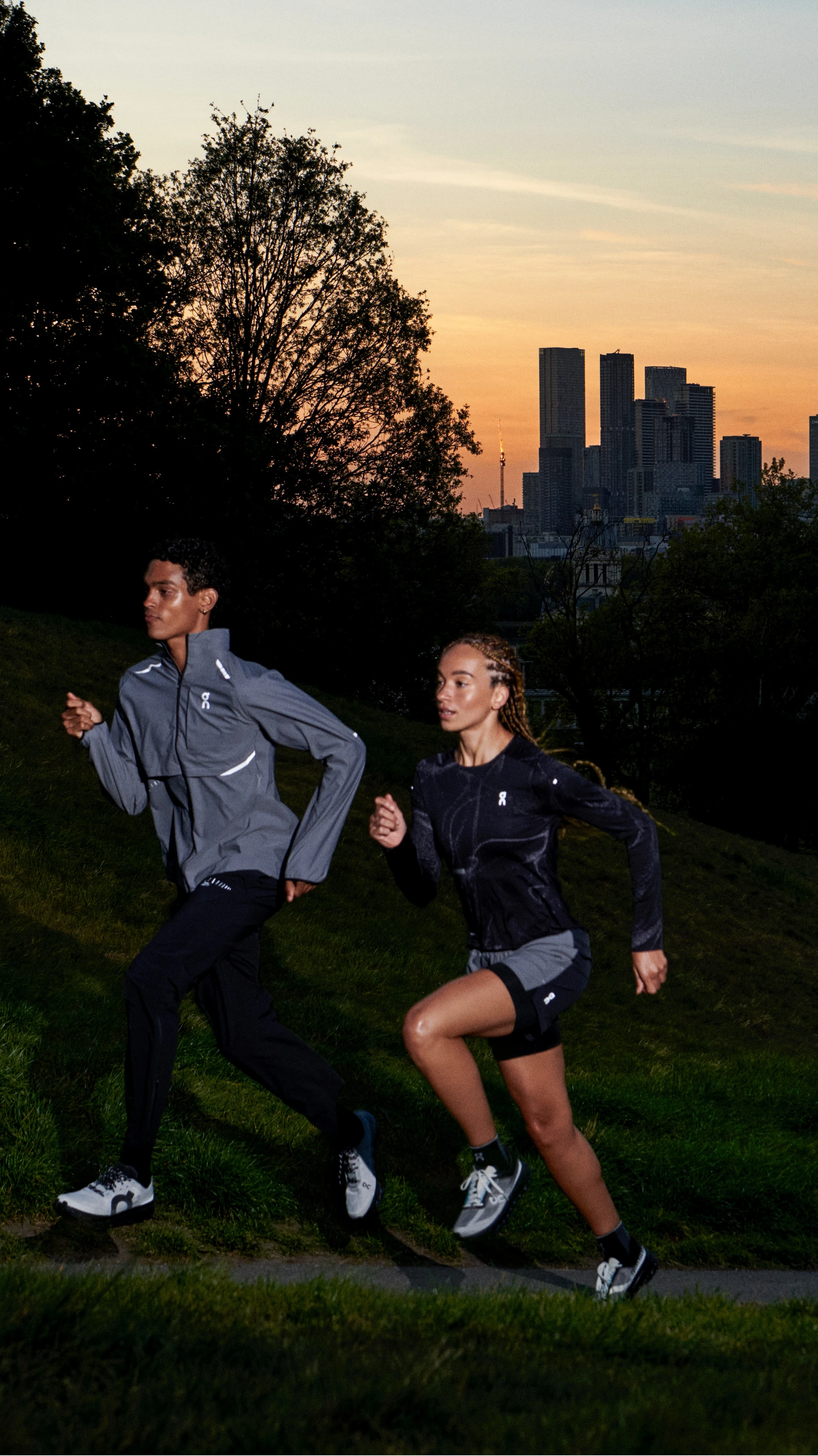 Two runners running uphill at sunrise with the city in the background.